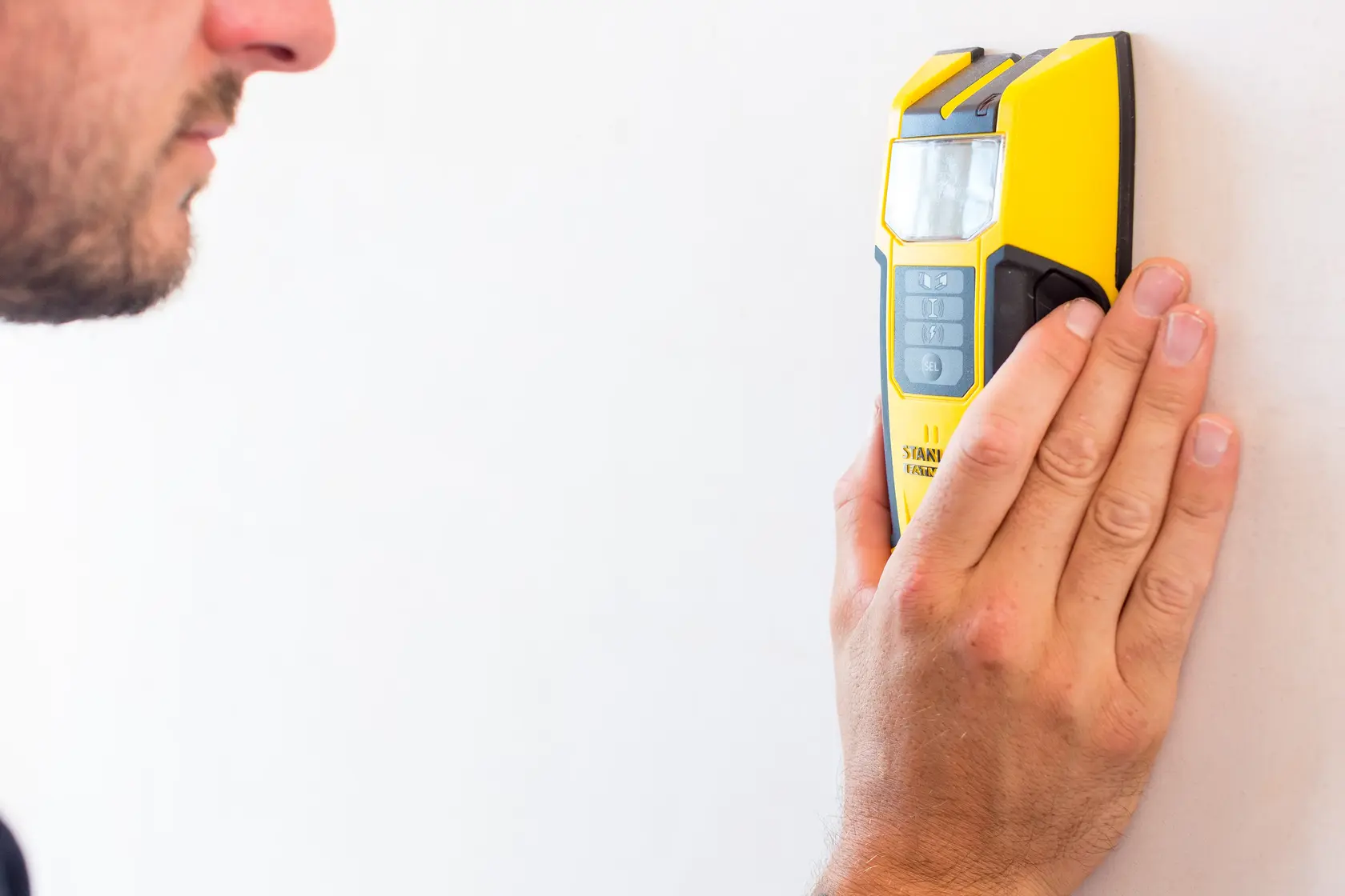 STANLEY FMHT0-77407 gelber elektronischer Leitungssucher von einer Person an eine weiße Wand gehalten.