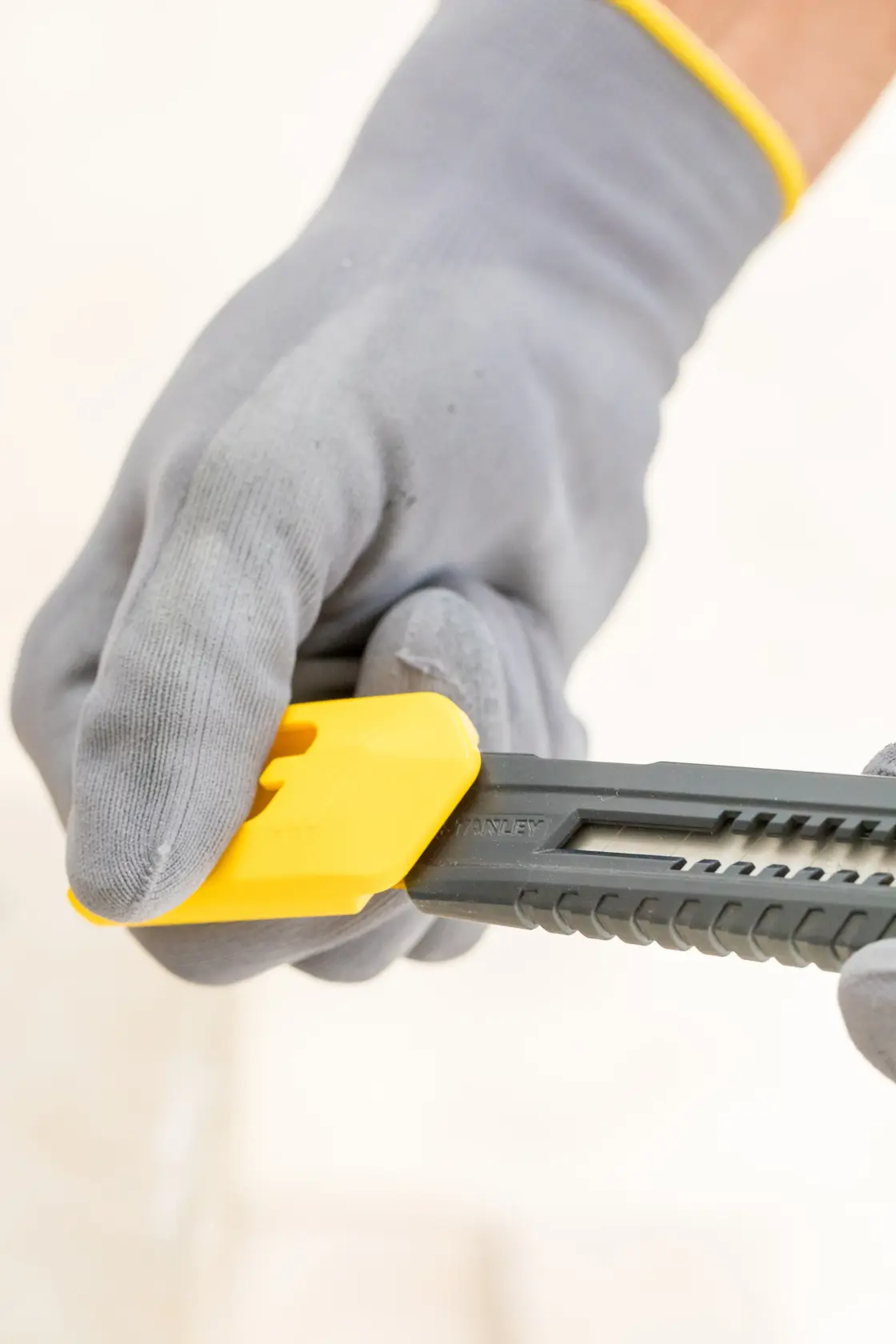 STANLEY 0-10-151 Universalmesser mit gelbem Schieber, gehalten von behandschuhter Hand, Nahaufnahme seitlich.