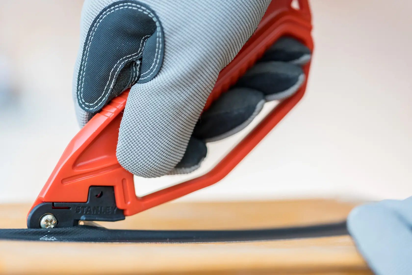 Photo of STANLEY 0-10-244 safety knife with red handle in use, close-up cutting a black material.