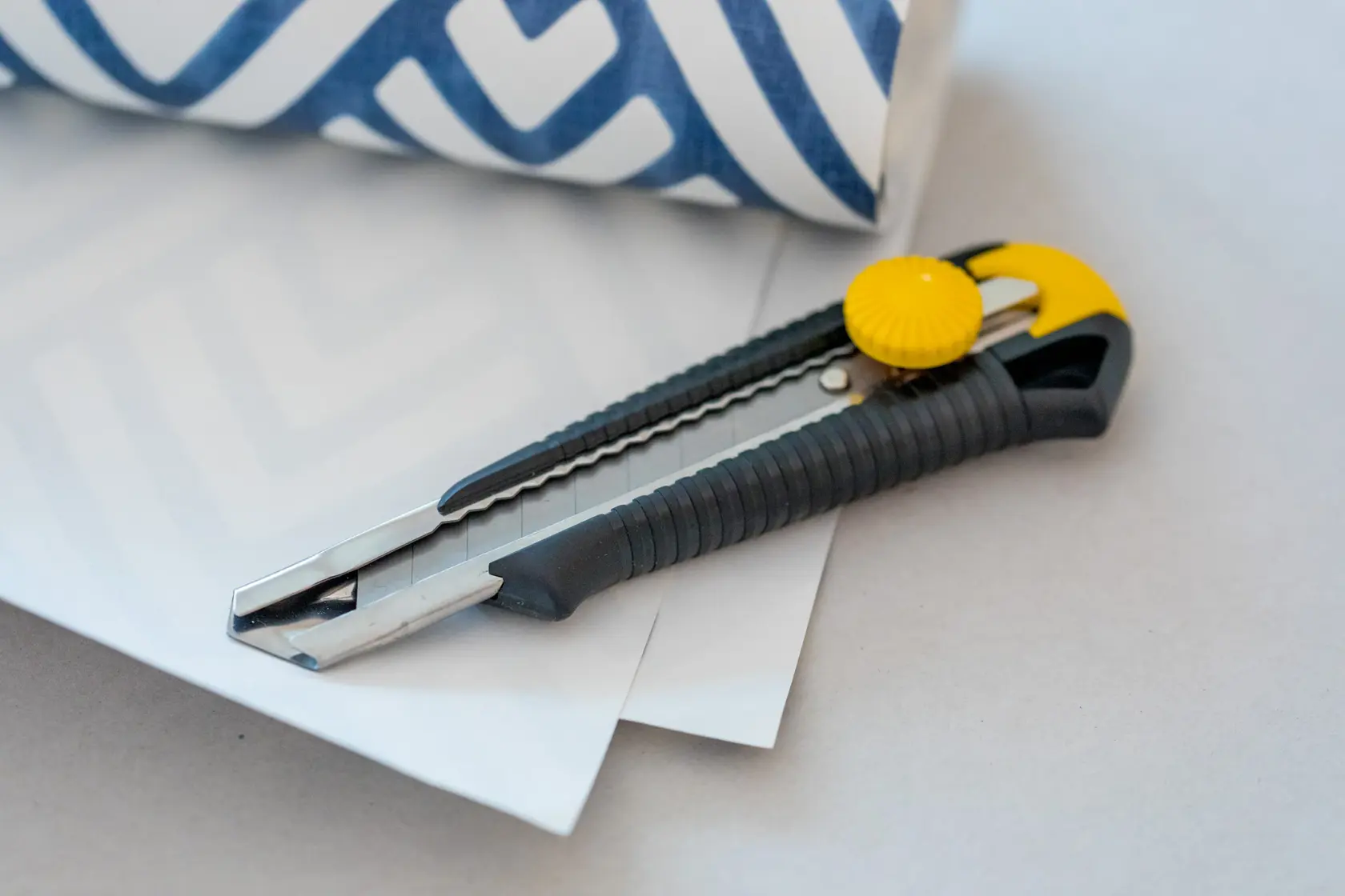 STANLEY 0-10-418 Universalmesser mit schwarzem und gelbem Griff, auf weißem Papier neben blau gemustertem Rolle.