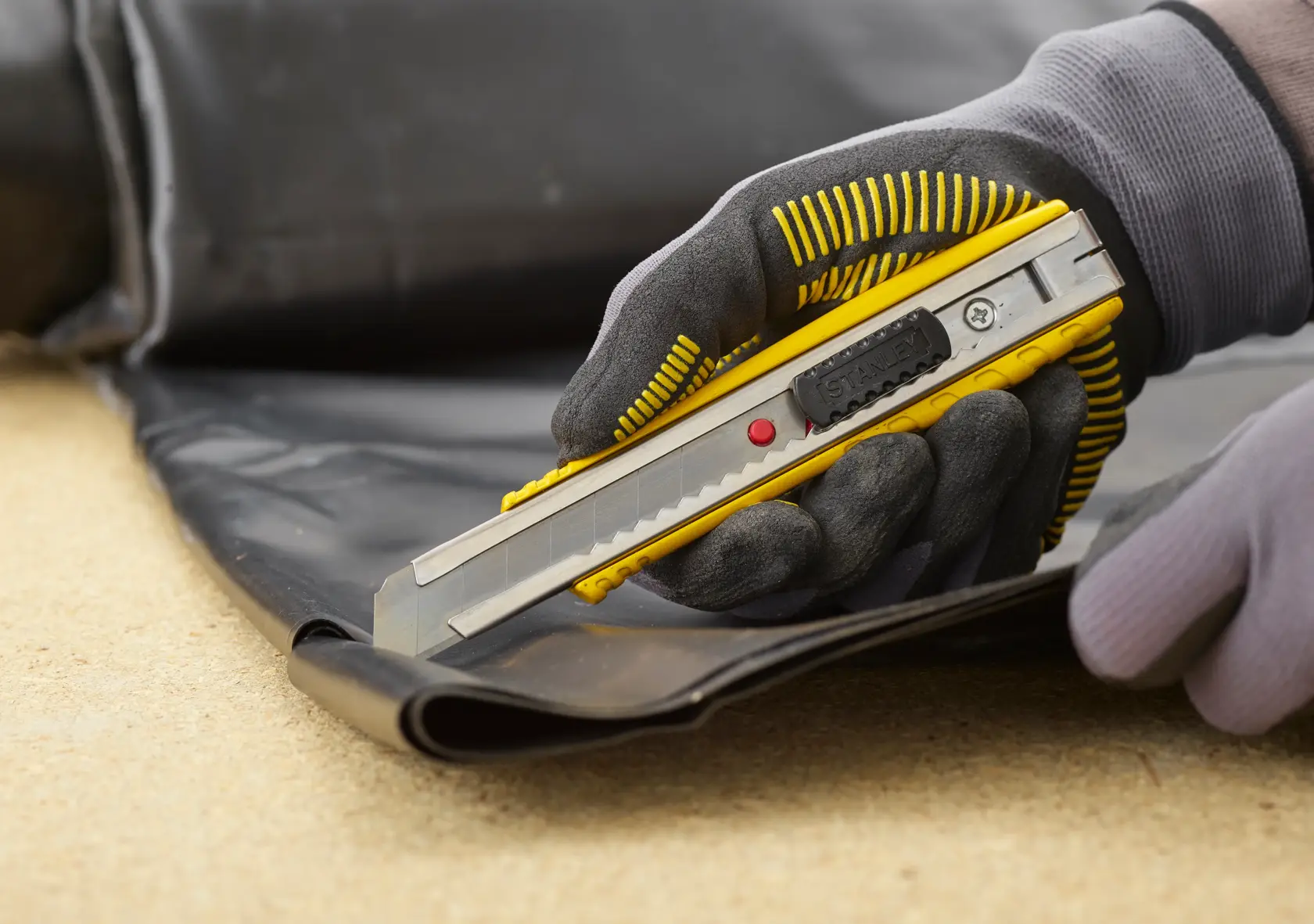STANLEY 0-10-431 Universalmesser schneidet schwarzes Material, Nahaufnahme einer behandschuhten Hand.