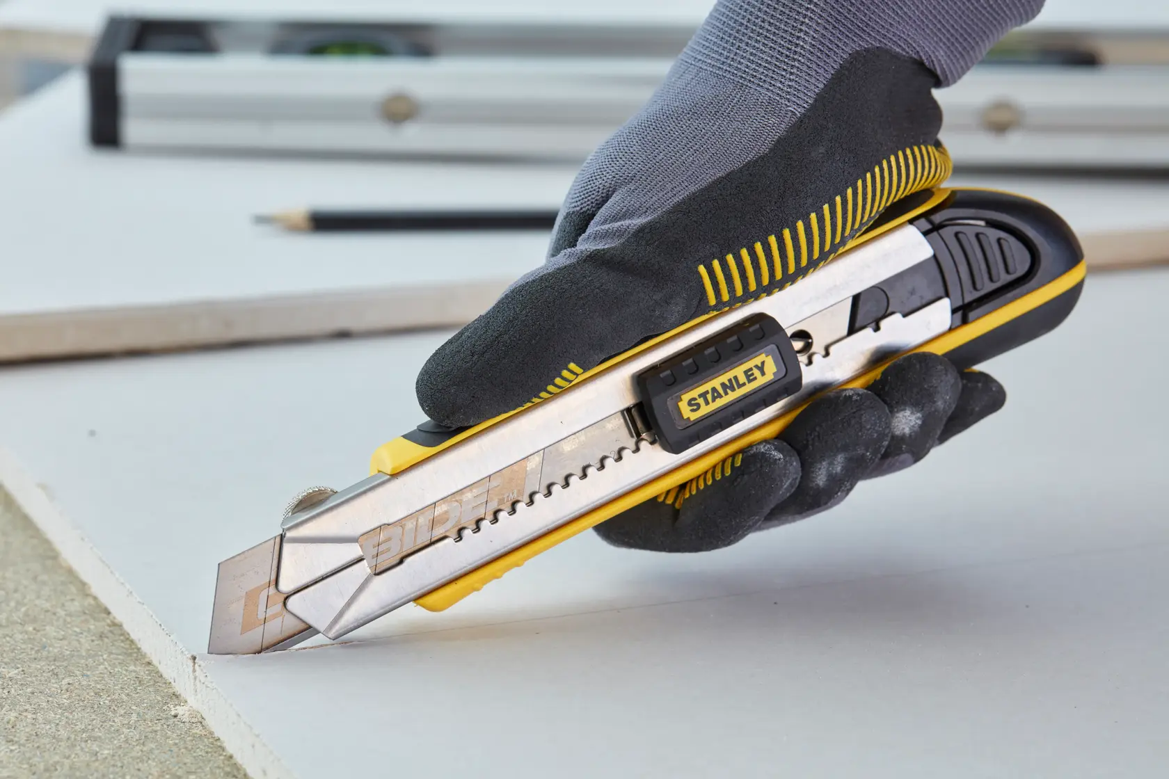 Foto: STANLEY 0-10-481 Cutter-Messer in behandschuhter Hand schneidet Trockenbauplatte, Seitenansicht.