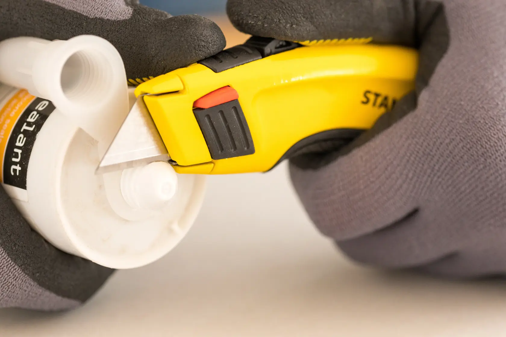 STANLEY 0-10-778 Messer schneidet Kunststoffrohr, Nahaufnahme, mit Handschuhen.