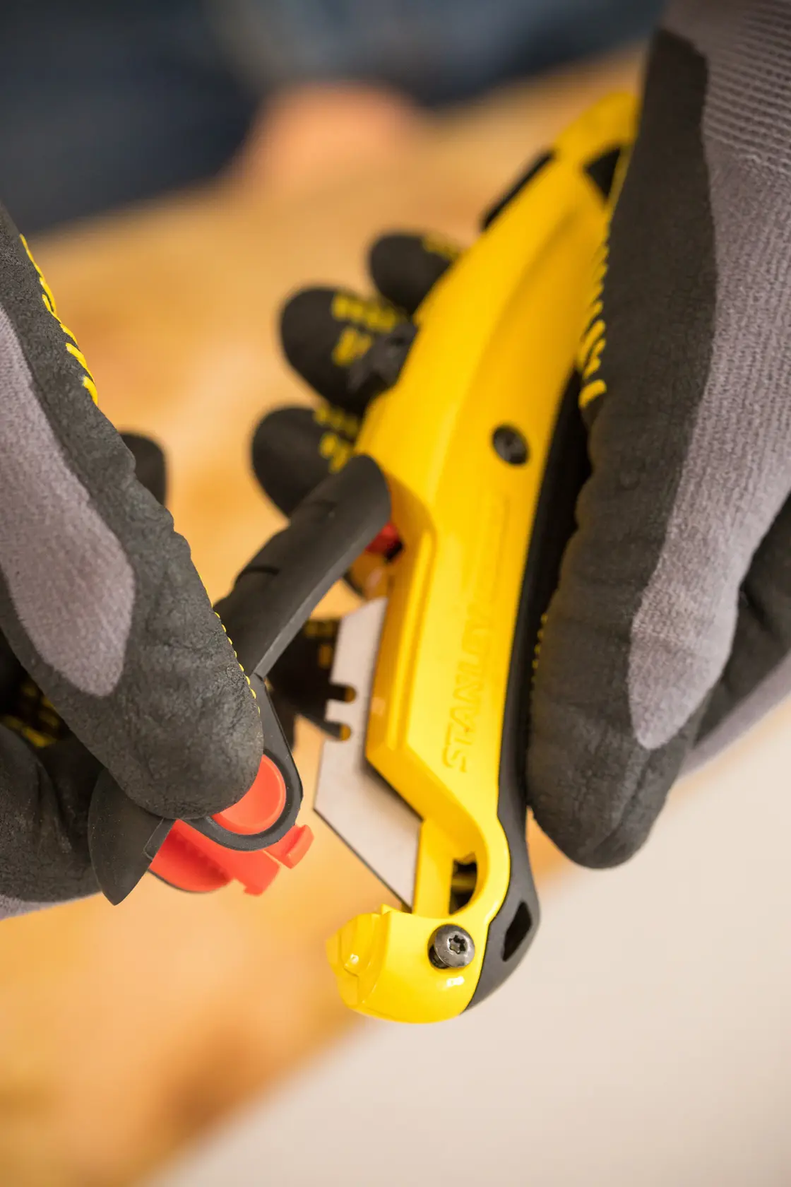 Foto vom STANLEY 0-10-778 Universalmesser, gelb-schwarzer Griff, Handschuhe, Nahaufnahme.