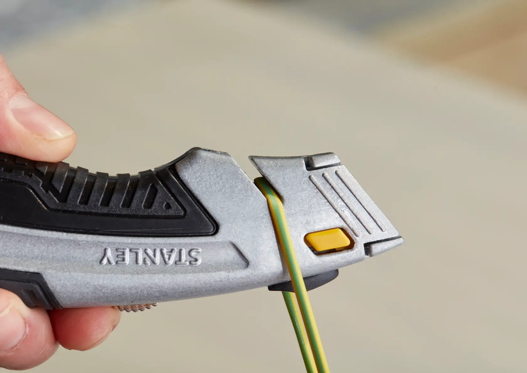 STANLEY 0-10-788 Universalmesser Nahaufnahme, silber und schwarz mit gelbem Knopf, schneidet grünes und gelbes Kabel.