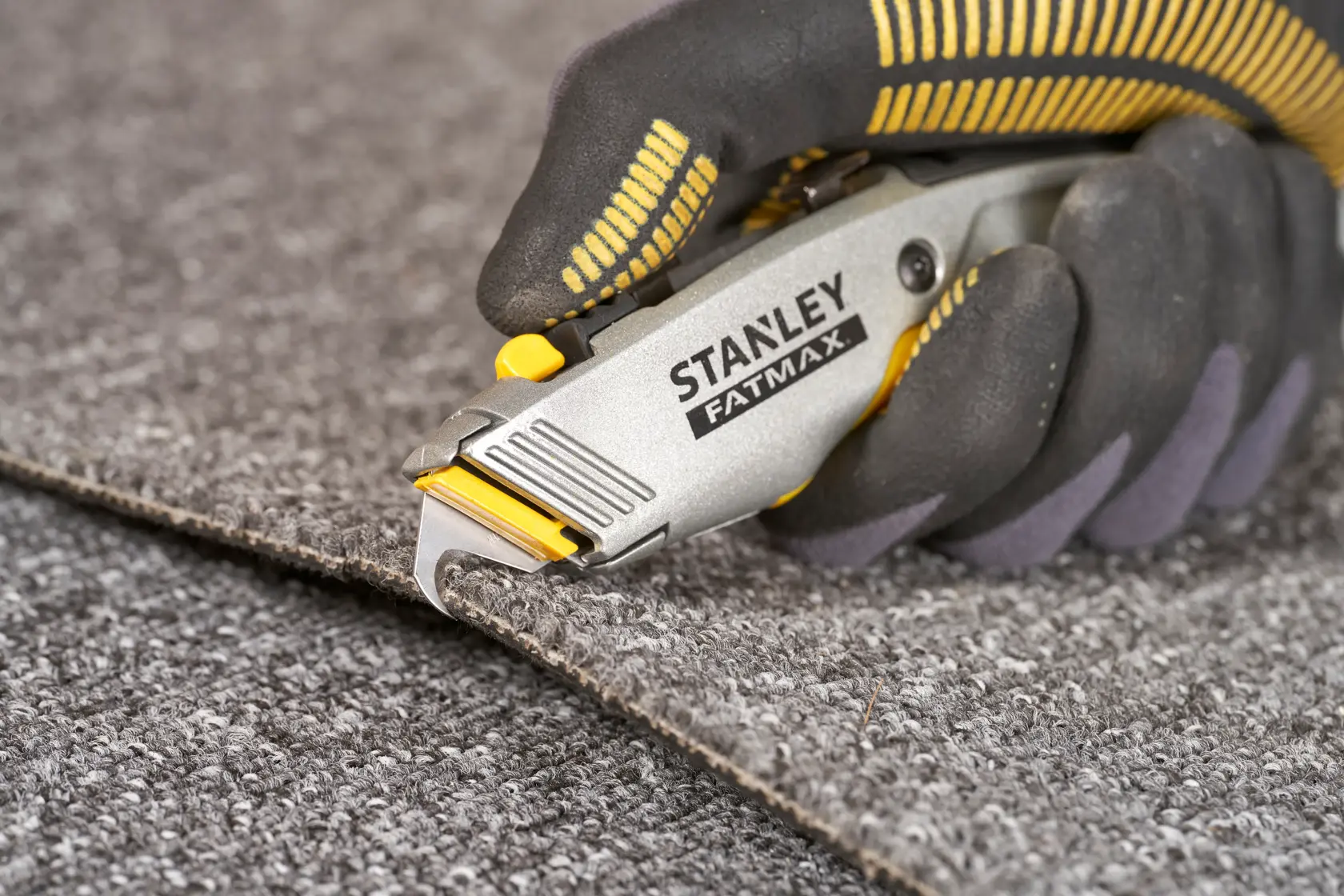 STANLEY 0-10-789 Universalmesser schneidet Teppich, Nahaufnahme, grauer und gelber Griff.