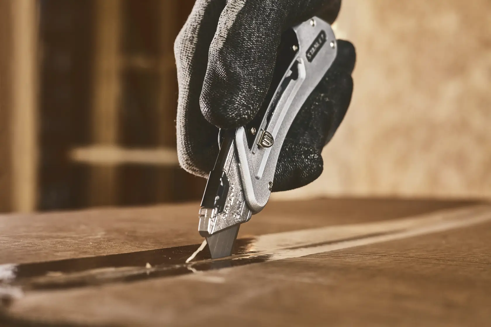 STANLEY 0-10-810 Universalmesser schneidet Karton, Nahaufnahme mit behandschuhter Hand, Produktfoto.