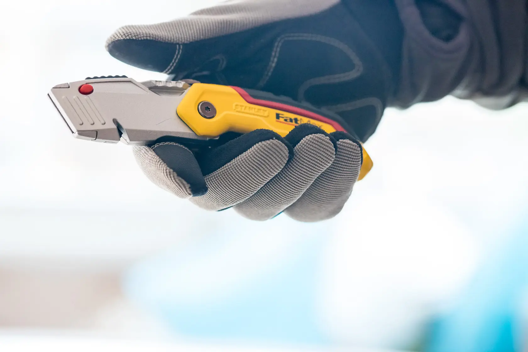 STANLEY 0-10-825 Universalmesser in einer behandschuhten Hand, gelber und silberner Griff sichtbar.