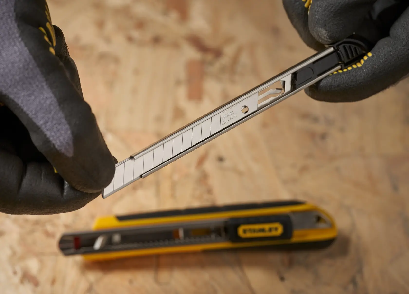 Foto von STANLEY 0-11-300 Abbrechklinge in der Hand, gelbes Cuttermesser darunter auf Holz.