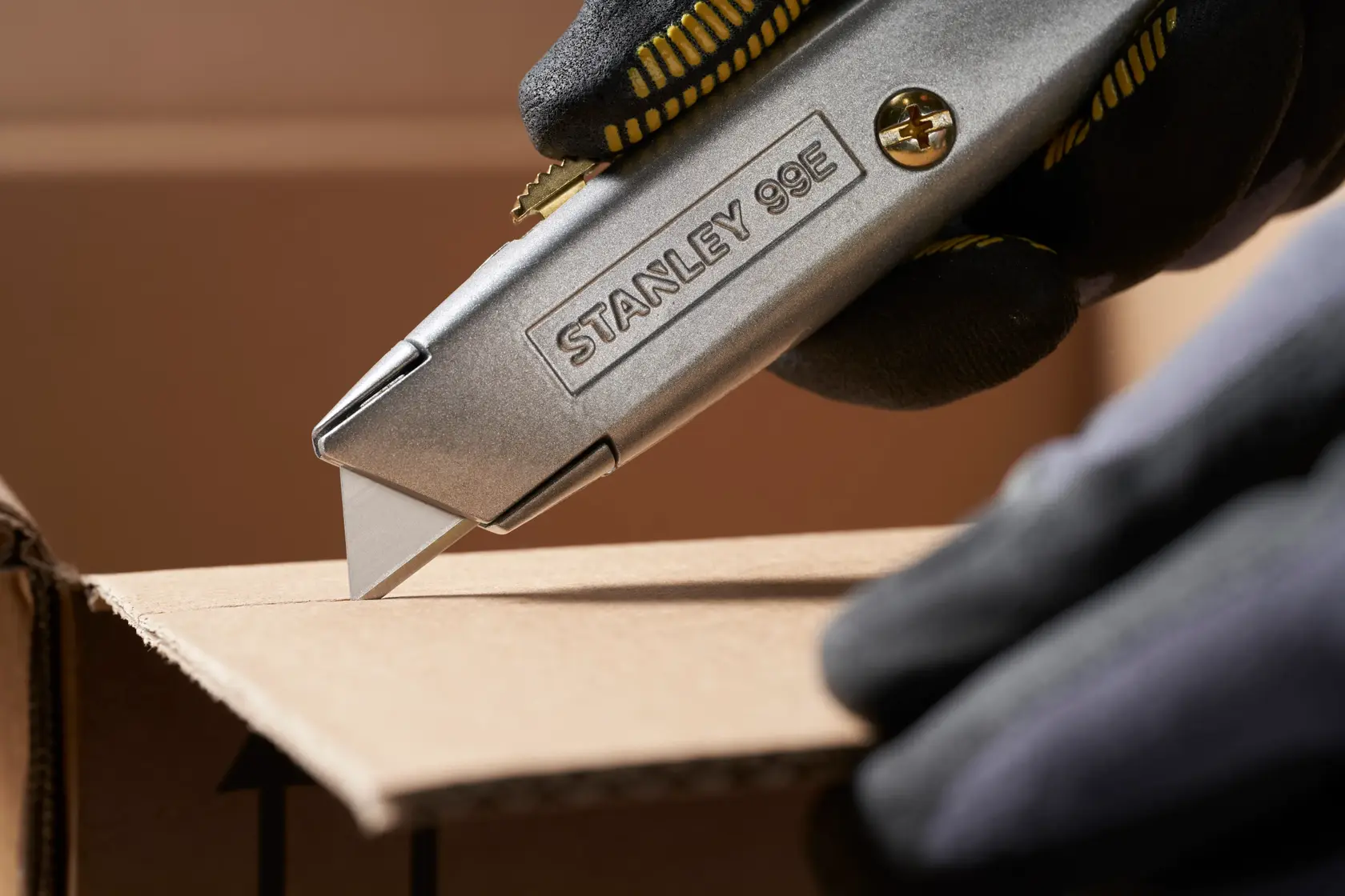STANLEY 0-11-911 Universalmesser schneidet Karton, Nahaufnahme von der Seite, Arbeiter trägt schwarze Handschuhe.