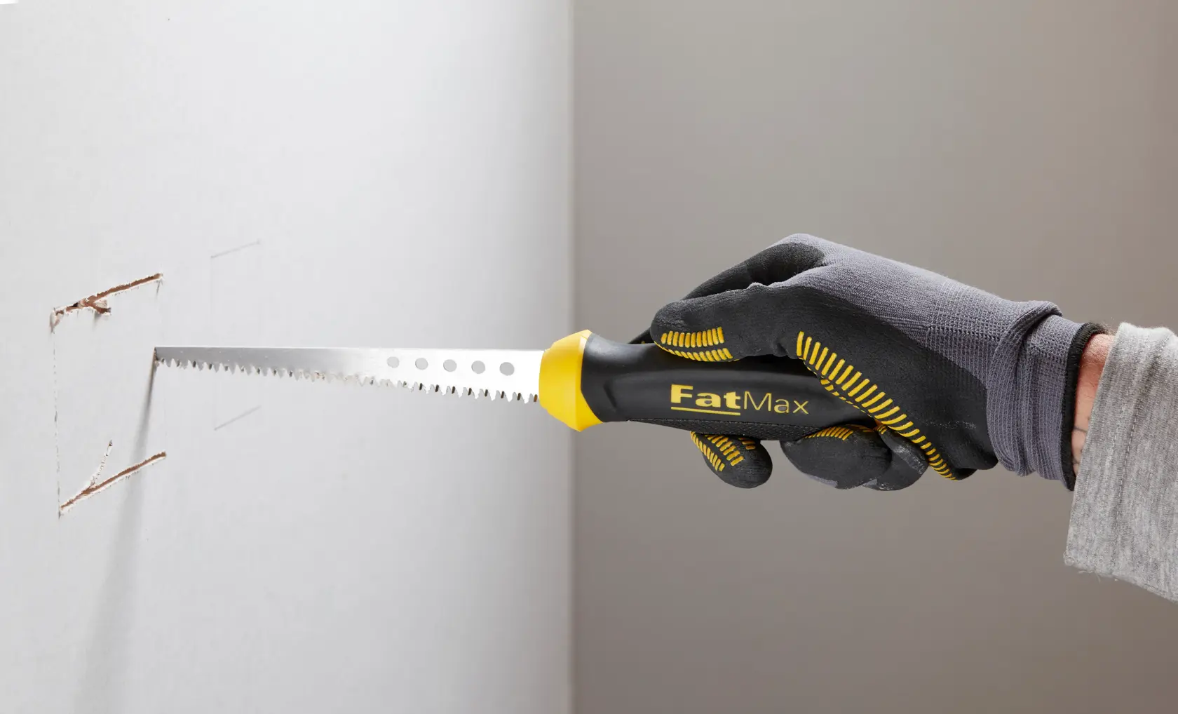 STANLEY 0-20-556 Handsäge mit schwarzem und gelbem FatMax Griff schneidet Trockenbauwand, Nahaufnahme Fotografie.