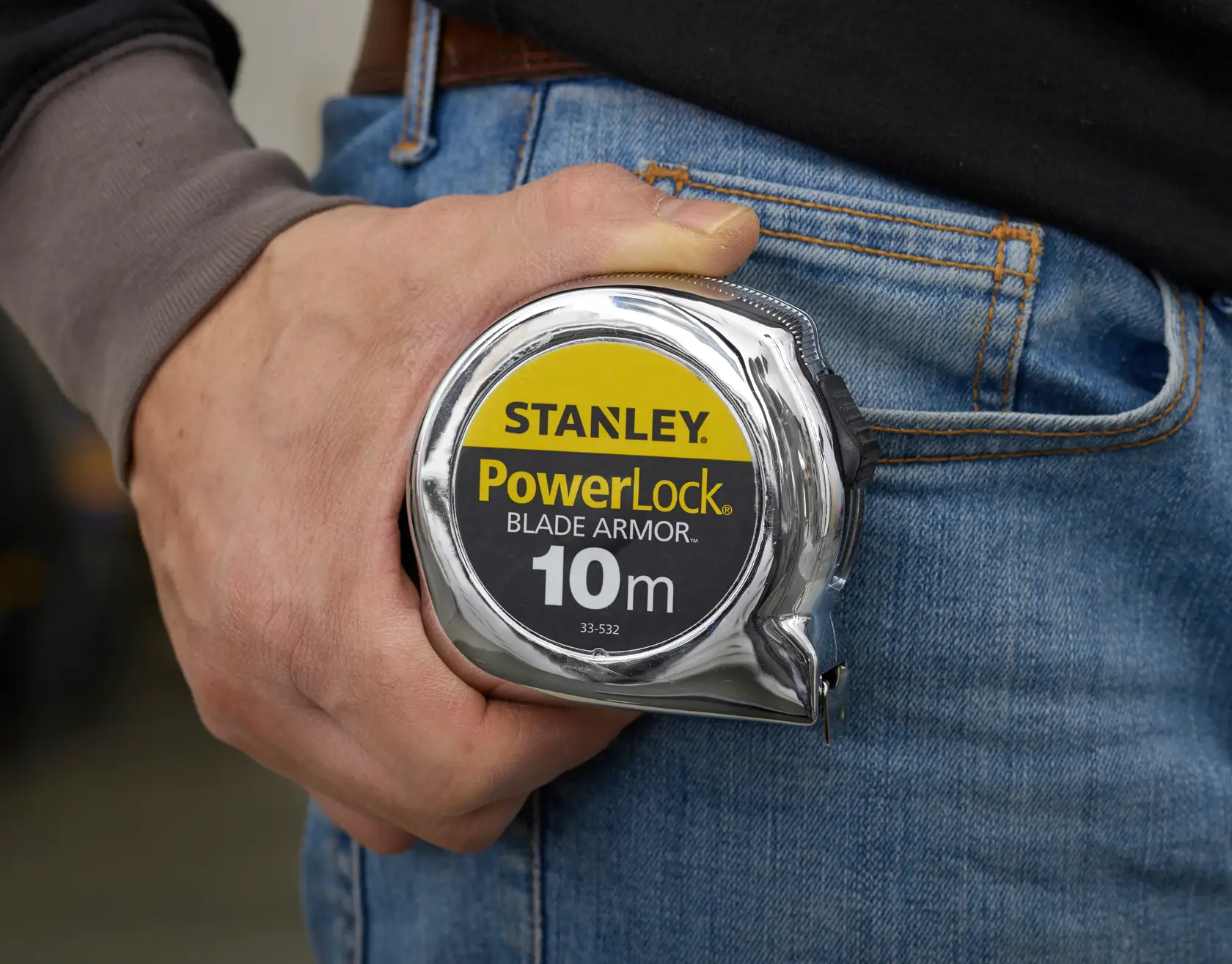 Foto vom STANLEY PowerLock Blade Armor 10m Maßband SKU 0-33-532 in einer Hand neben blauer Jeans.