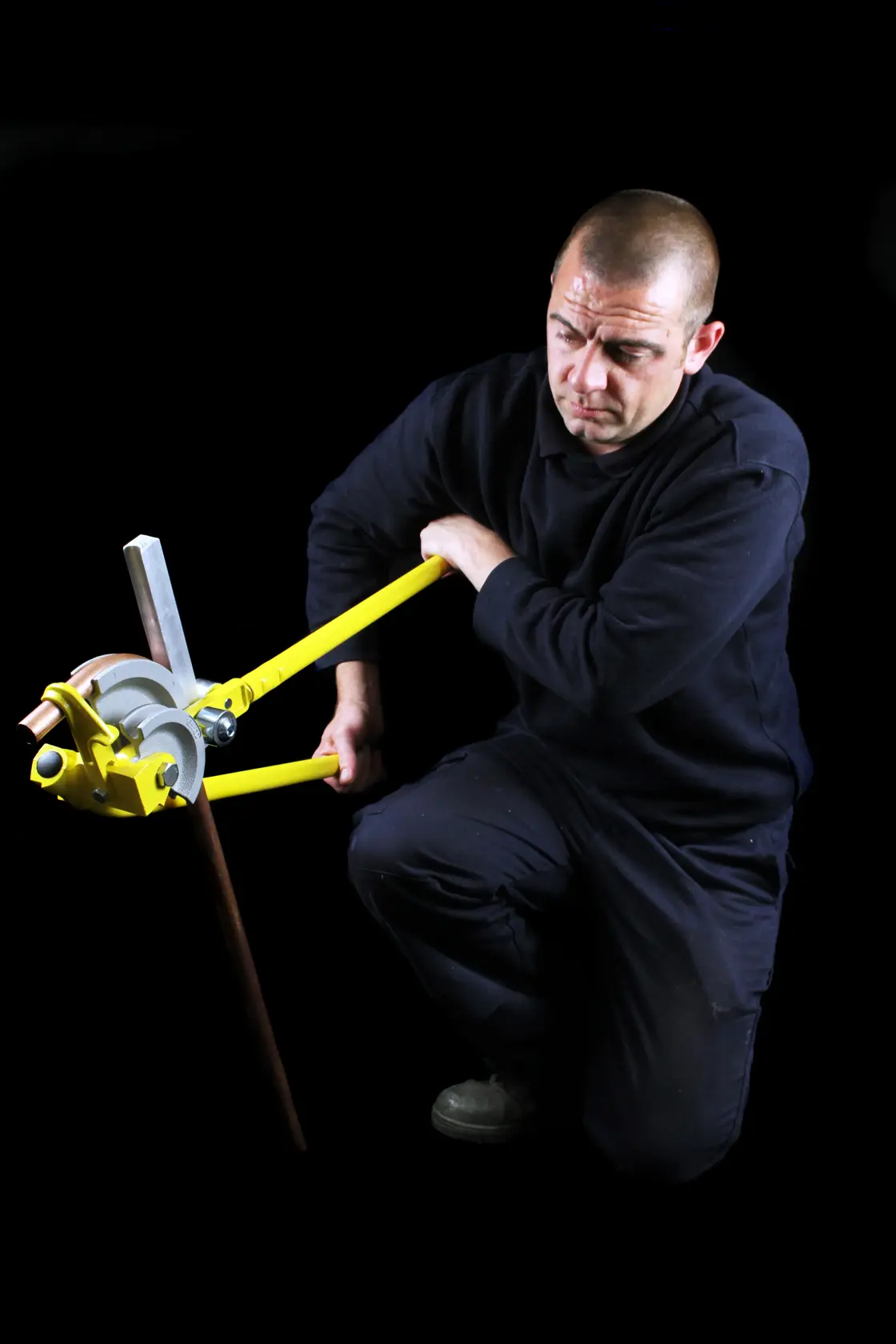 Fotografie einer Person mit dem STANLEY 0-70-452 Rohrbieger an einem Metallrohr, vor schwarzem Hintergrund.