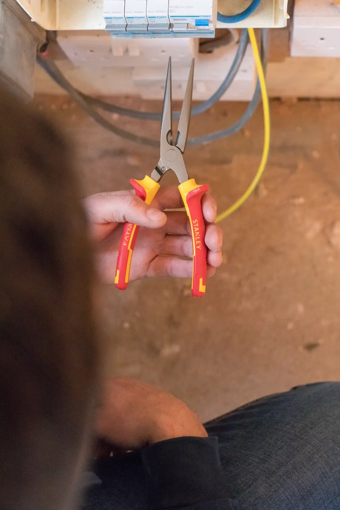 Foto von STANLEY 0-84-007 isolierten langen Spitzzange mit roten und gelben Griffen in der Hand, Elektrobereich.