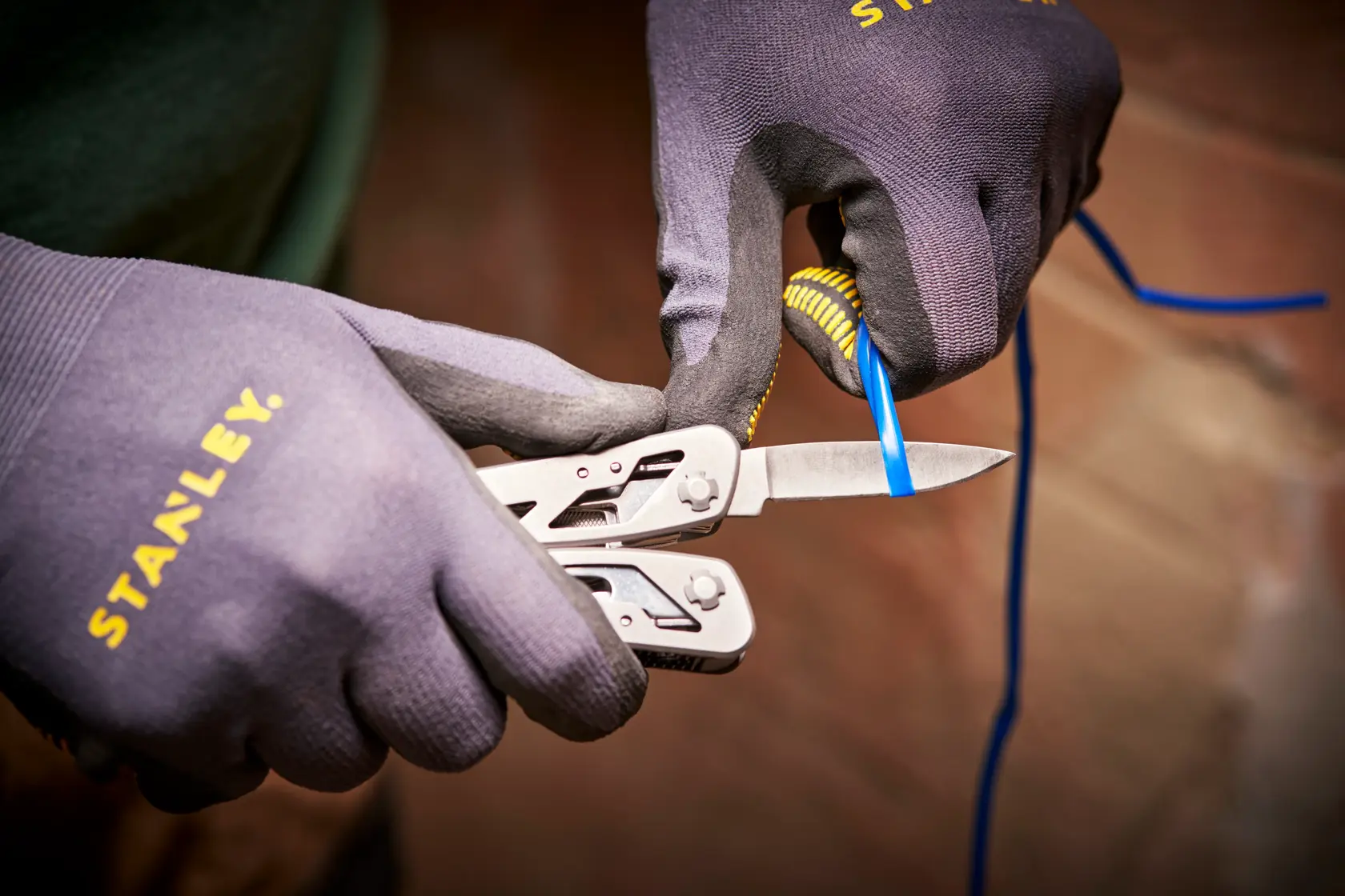 STANLEY 0-84-519 Multitool schneidet blauen Draht, Nahaufnahme, getragen mit STANLEY Handschuhen.