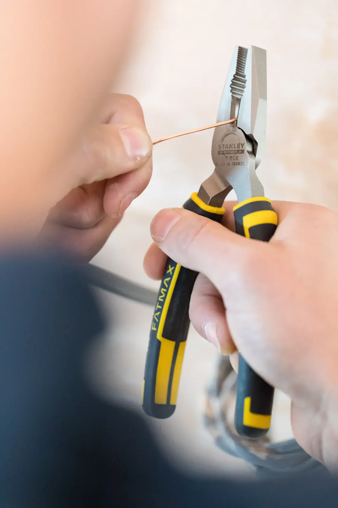 STANLEY 0-89-866 Zange mit schwarzen und gelben Griffen hält Kupferdraht, Nahaufnahme in der Hand.