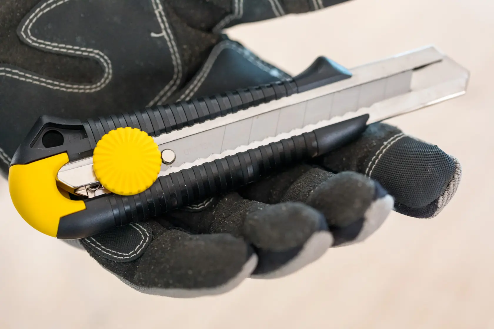 STANLEY 1-10-418 Universalmesser mit gelbem Drehknopf, gehalten in einer Handschuhhand, Nahaufnahme Fotografie.