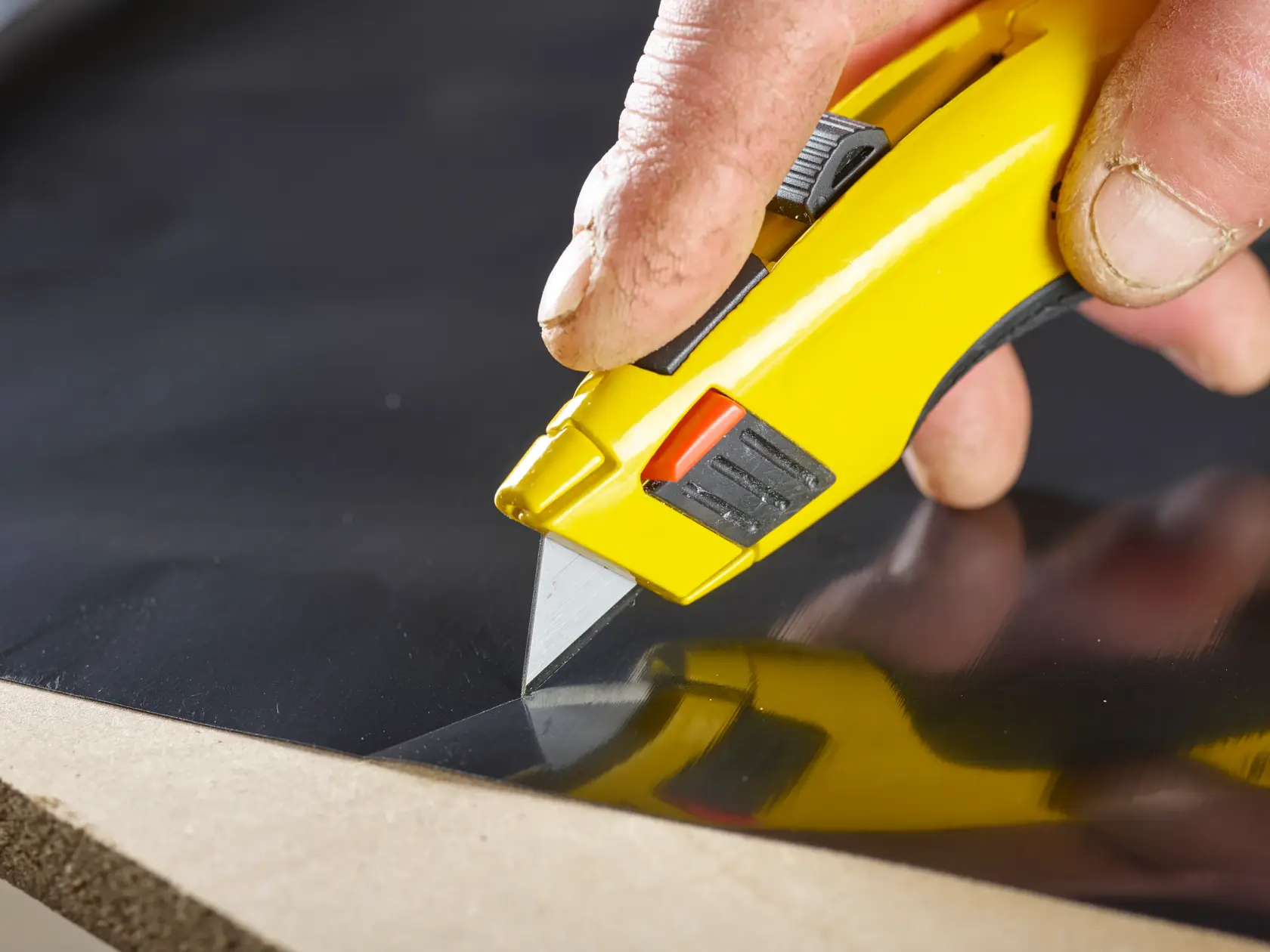 STANLEY 1-11-921 Universalmesser schneidet schwarzes Material, Nahaufnahme von gelbem Griff und Klinge im Einsatz.