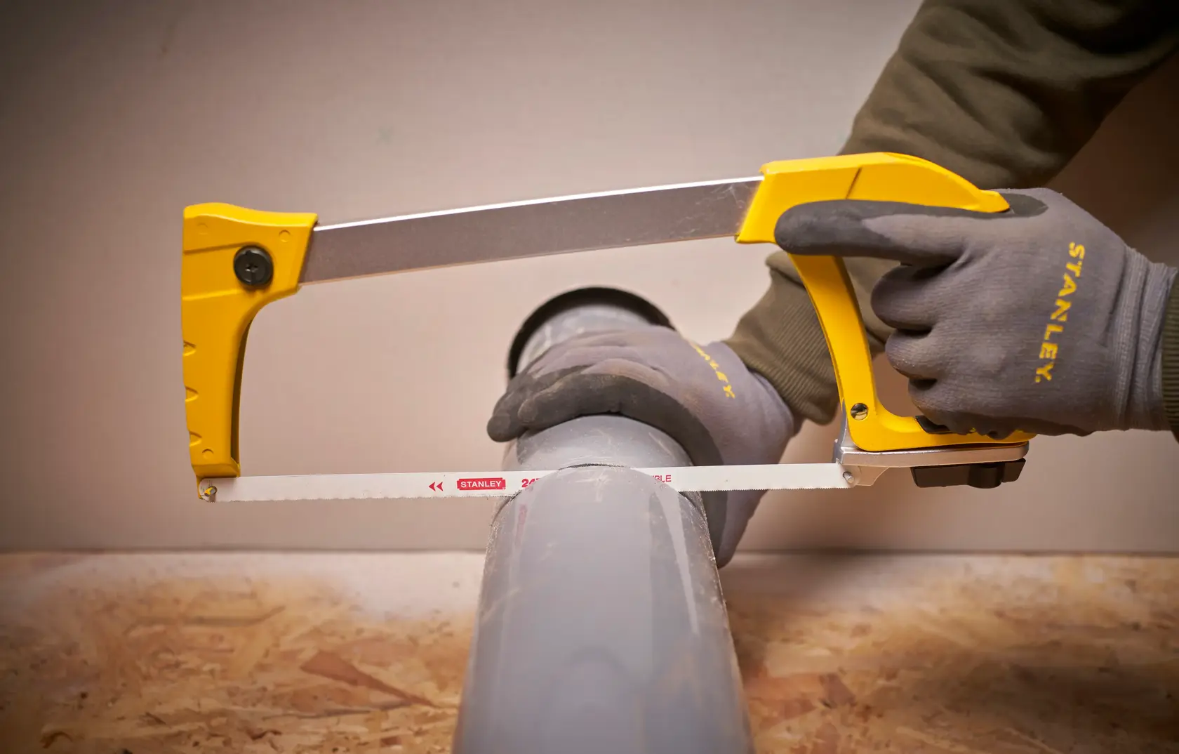STANLEY 1-20-110 Bügelsäge schneidet graues Rohr, Nahaufnahme, Arbeiter mit STANLEY-Handschuhen.