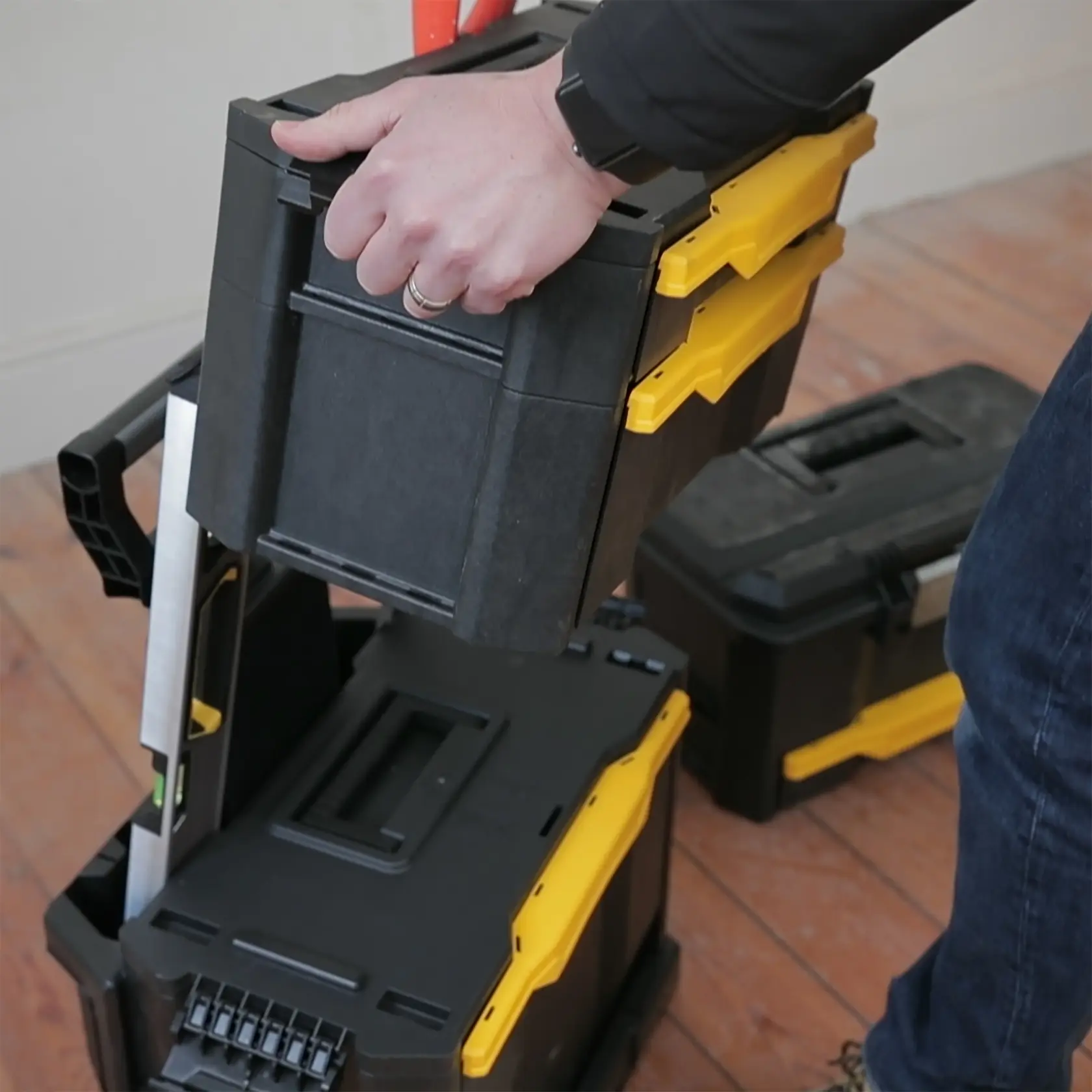STANLEY 1-79-206 schwarze und gelbe stapelbare Werkzeugbox wird auf Holzfußboden getragen und sortiert.