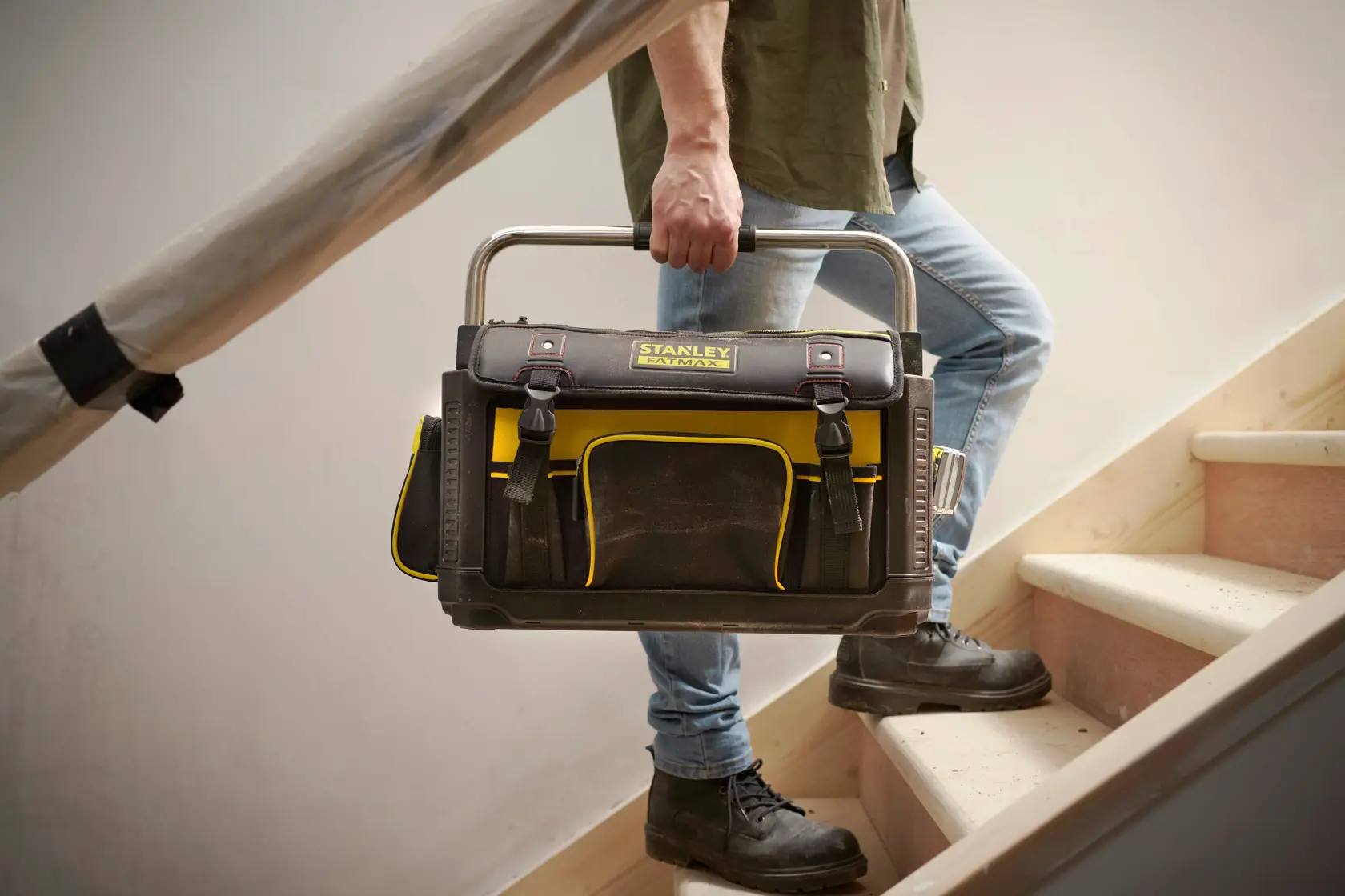 STANLEY 1-79-213 Werkzeugtasche in Schwarz und Gelb, Fotografie getragen von einer Person auf einer Treppe.