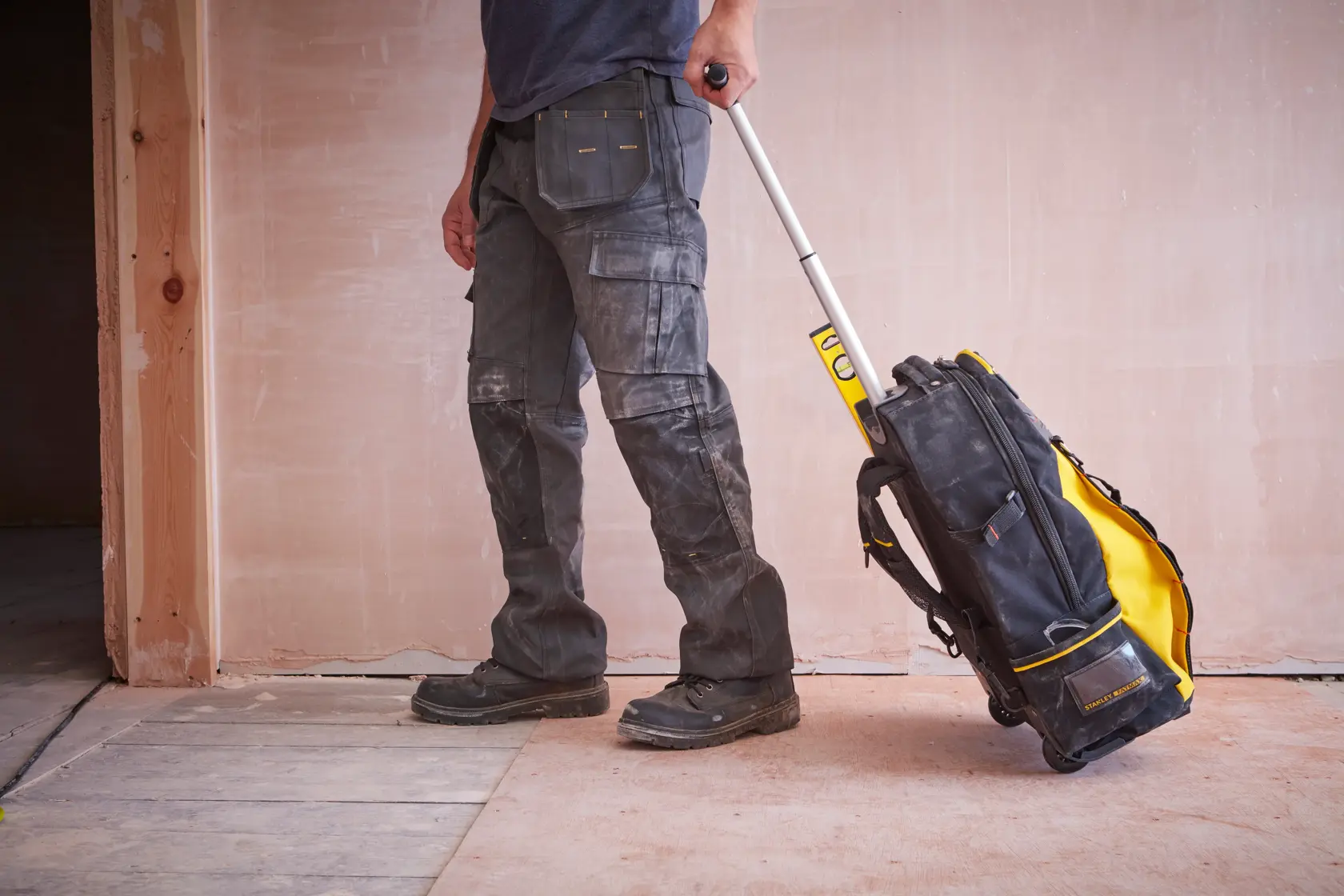 STANLEY 1-79-215 Rollwerkzeugtasche in Gelb und Schwarz, ausgezogener Griff, auf Baustellenboden im Einsatz.