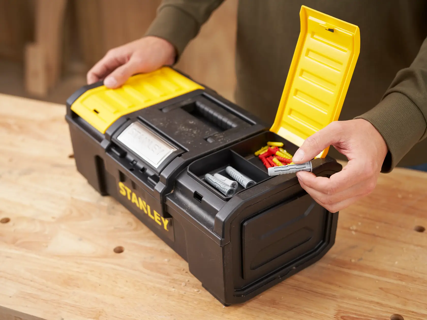 STANLEY 1-79-216 schwarze und gelbe Werkzeugbox mit offenem Deckel und Dübeln in Fächern auf Werkbank.