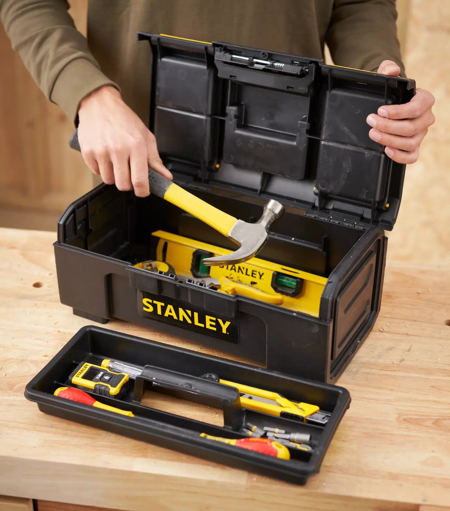Foto von STANLEY 1-79-216 Werkzeugkasten mit gelben Werkzeugen, offen, Person hält Hammer.