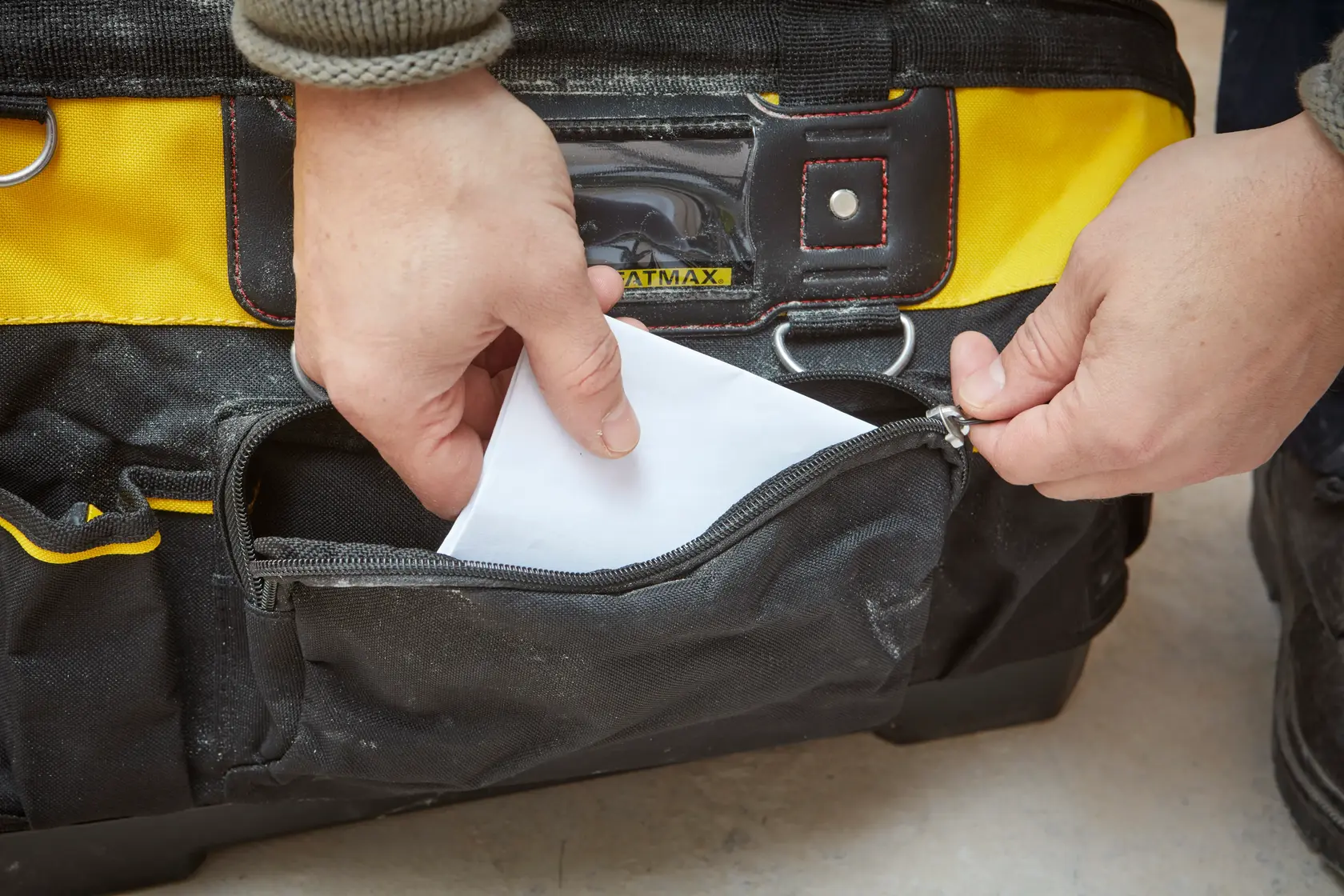 Foto der STANLEY 1-93-950 Werkzeugtasche mit offener Reißverschlusstasche, Hand steckt Papier hinein, Nahaufnahme.