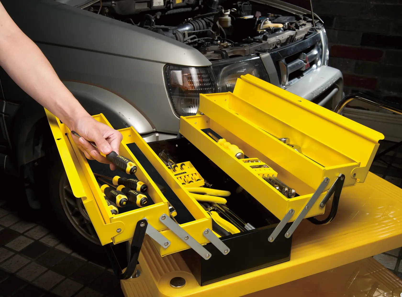 STANLEY 1-94-738 gelber Metall-Werkzeugkasten offen mit Werkzeugen, neben Auto, Seitenansicht.