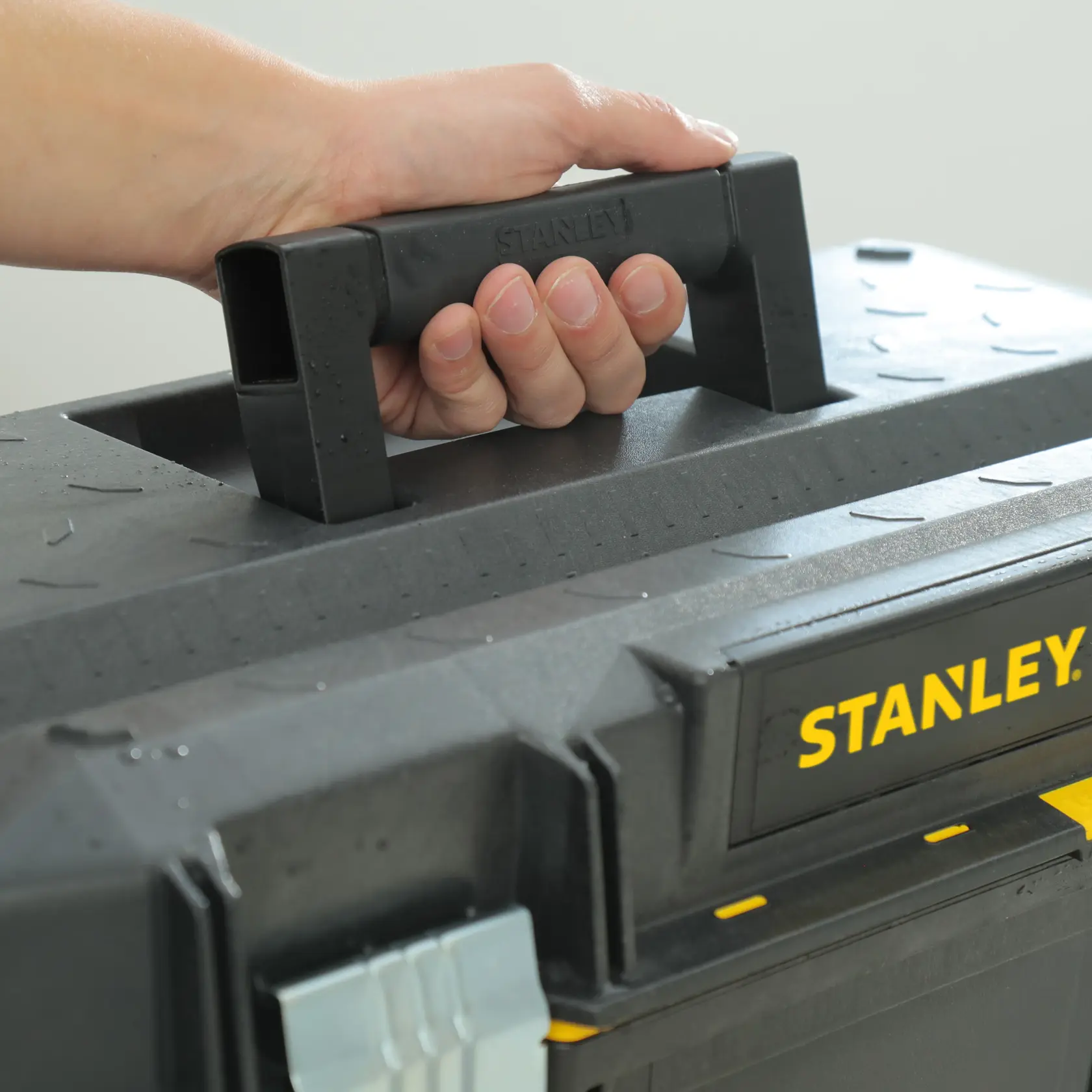 STANLEY 1-94-749 schwarzer Werkzeugkasten-Griff Nahaufnahme, Hand hält, gelbes Logo sichtbar.