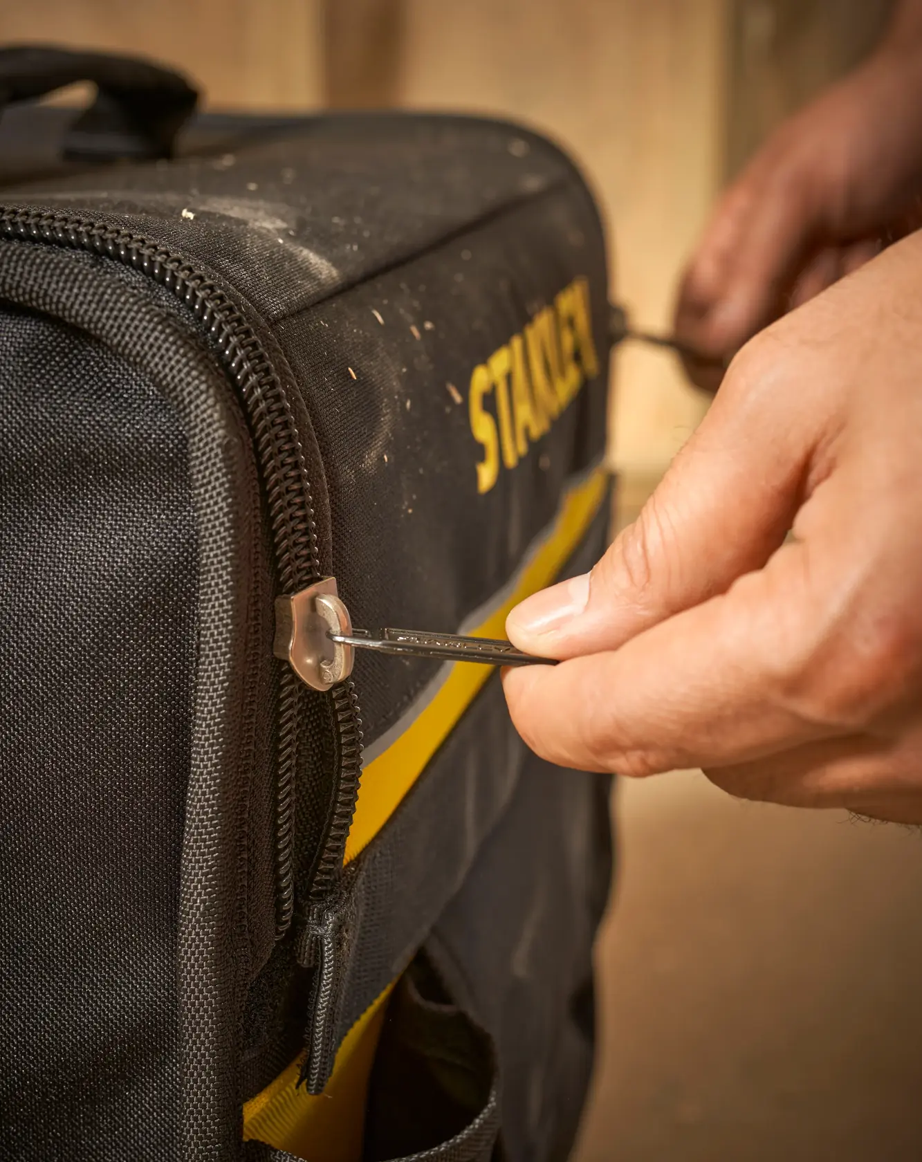 STANLEY 1-97-515 Werkzeugtasche Seitenansicht, Person öffnet schwarz-gelbe Tasche mit Metallreißverschluss.
