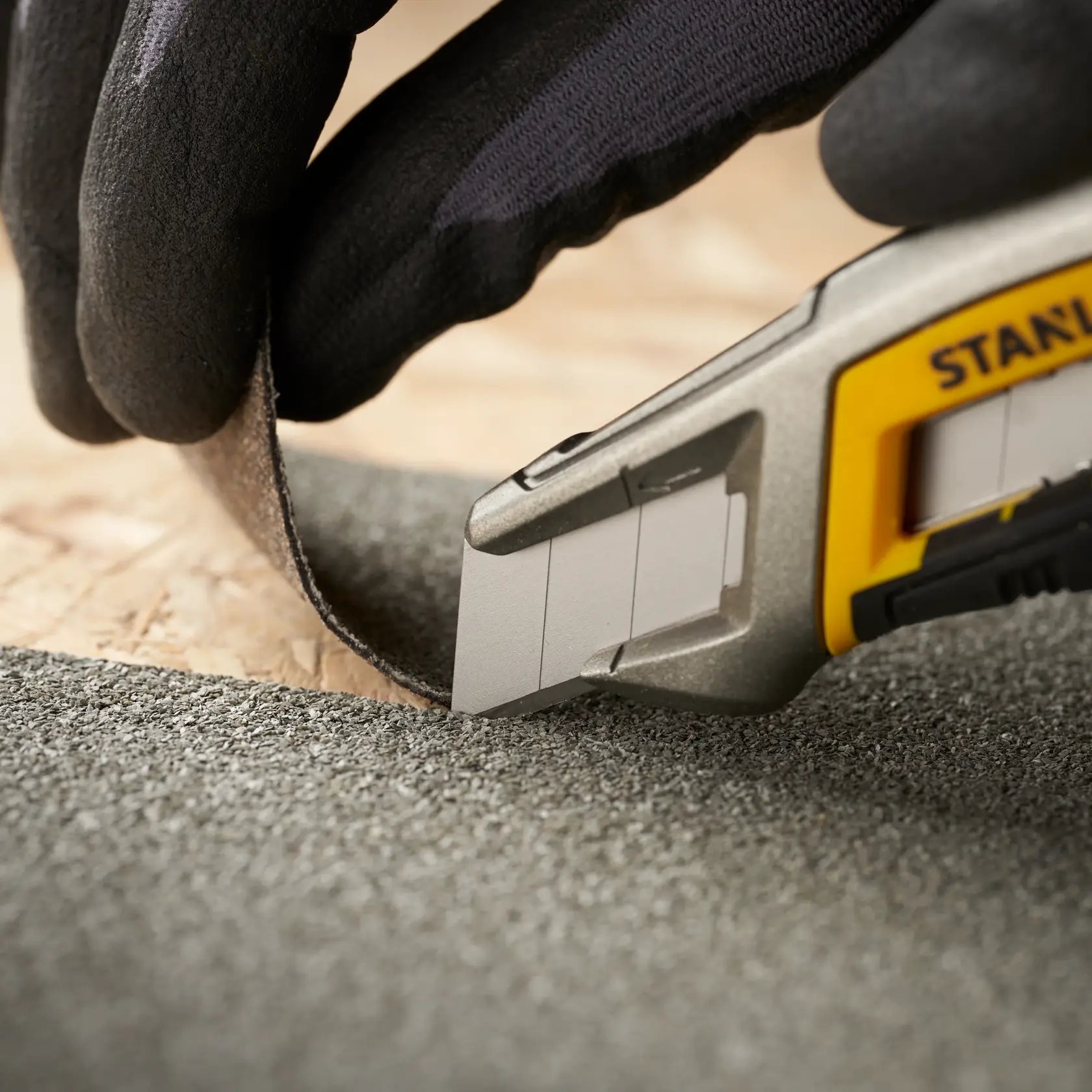 STANLEY 2-11-718 Universalmesser schneidet Dachmaterial, Nahaufnahme mit behandschuhter Hand, Produktfotografie.