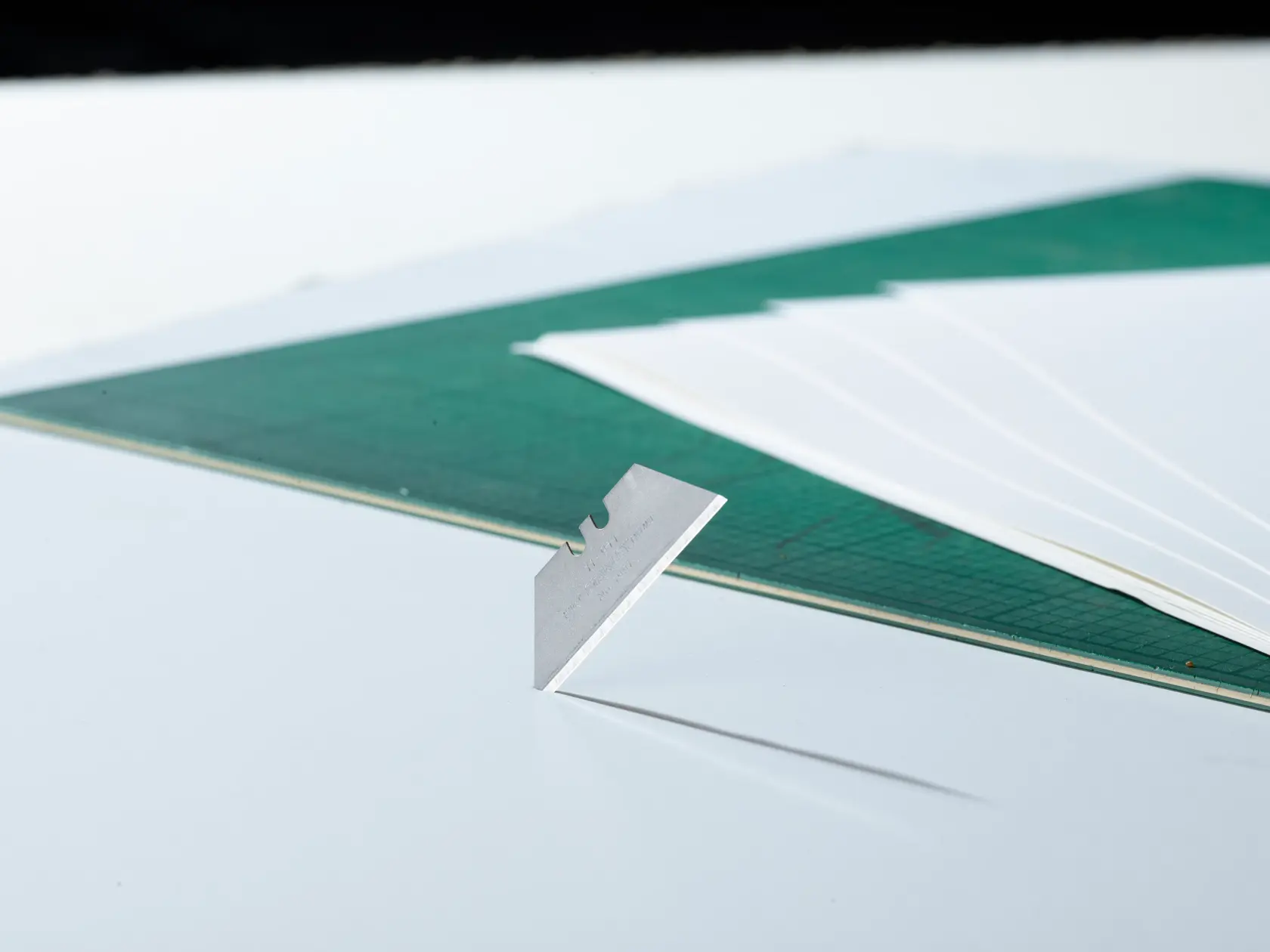 STANLEY 2-11-911 Universalklinge aufrecht auf weißer Fläche, mit grünem Schneidematte und Papier im Hintergrund.