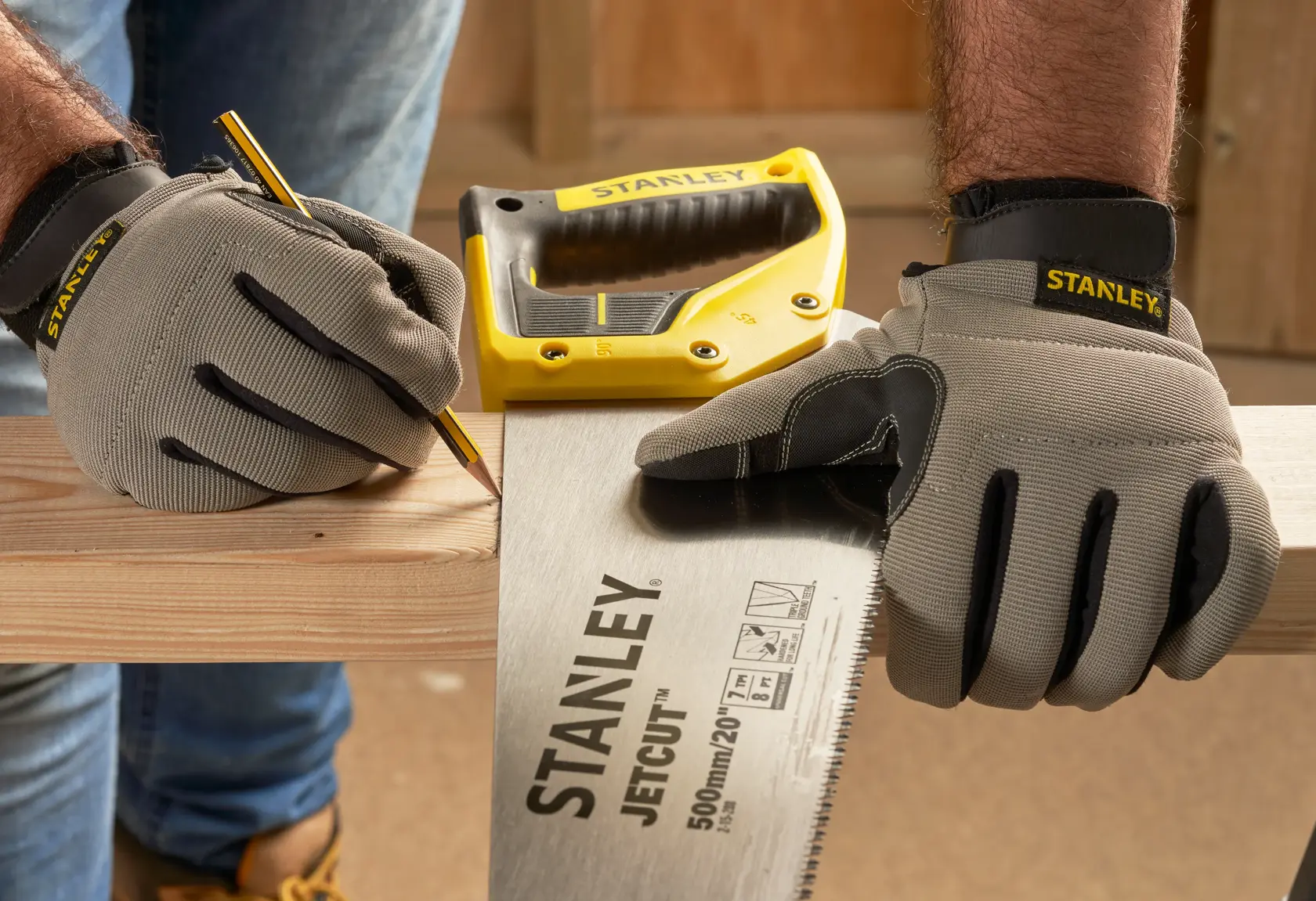 STANLEY 2-15-288 Handsäge und gelber Tacker auf Holz, Person mit Handschuhen markiert Schnittlinie, Werkstatt-Hintergrund.