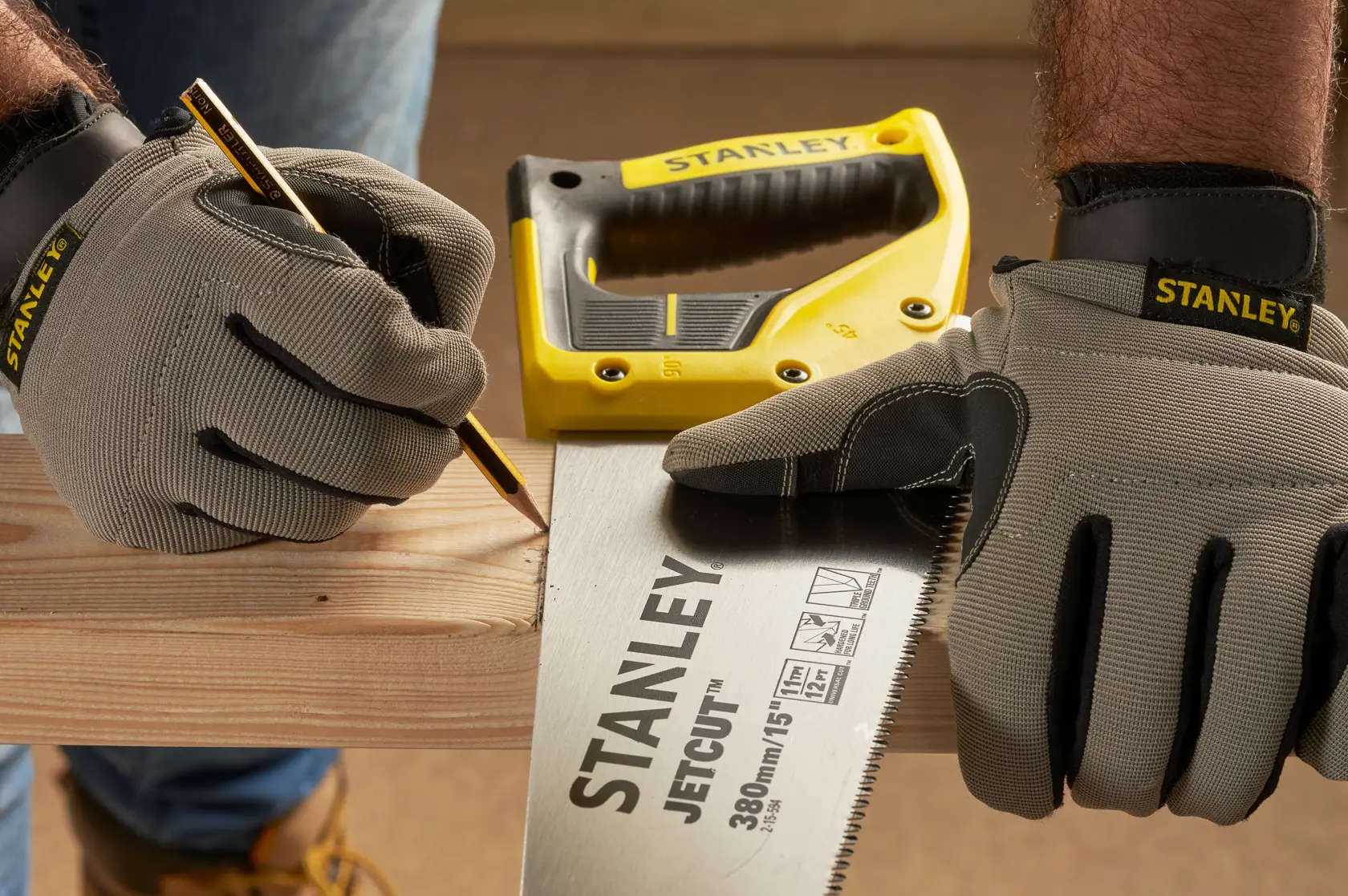 STANLEY 2-15-594 Handsäge im Einsatz, behandschuhte Hände markieren Holz, Bleistift und gelber Griff sichtbar.