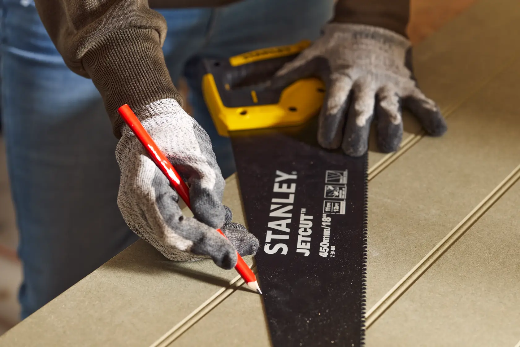 Fotografie der STANLEY 2-20-180 Handsäge, gehalten von behandschuhten Händen, markiert eine Linie auf Holz mit rotem Bleistift.