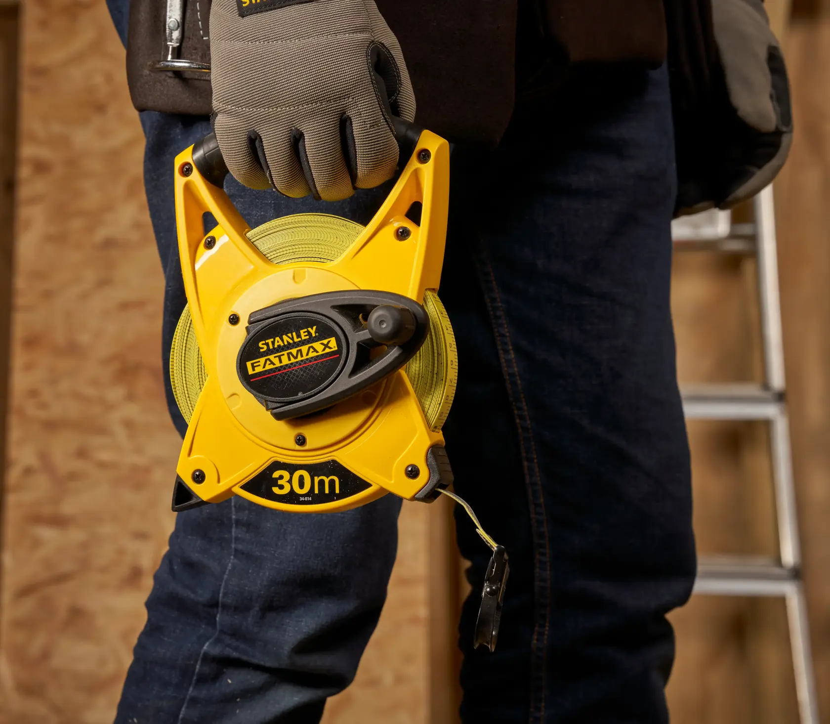STANLEY 2-34-814 FATMAX 30m Bandmaß mit offenem Gehäuse in behandschuhter Hand, Werkstatt-Hintergrund.