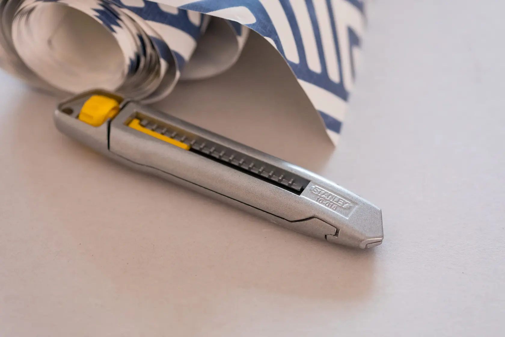 STANLEY 4-10-018 Universalmesser mit silbernem Gehäuse und gelbem Schieber neben gemustertem Papier.
