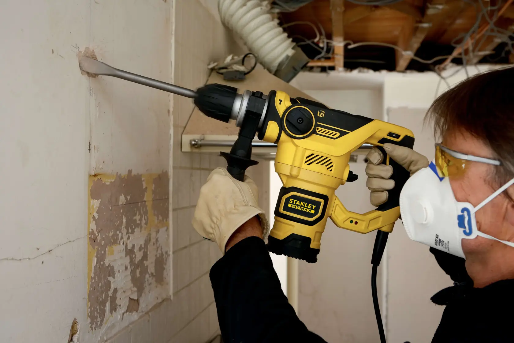 Foto einer Person mit dem STANLEY FME1250K Bohrhammer, bohrt in die Wand, mit Handschuhen und Schutzmaske.