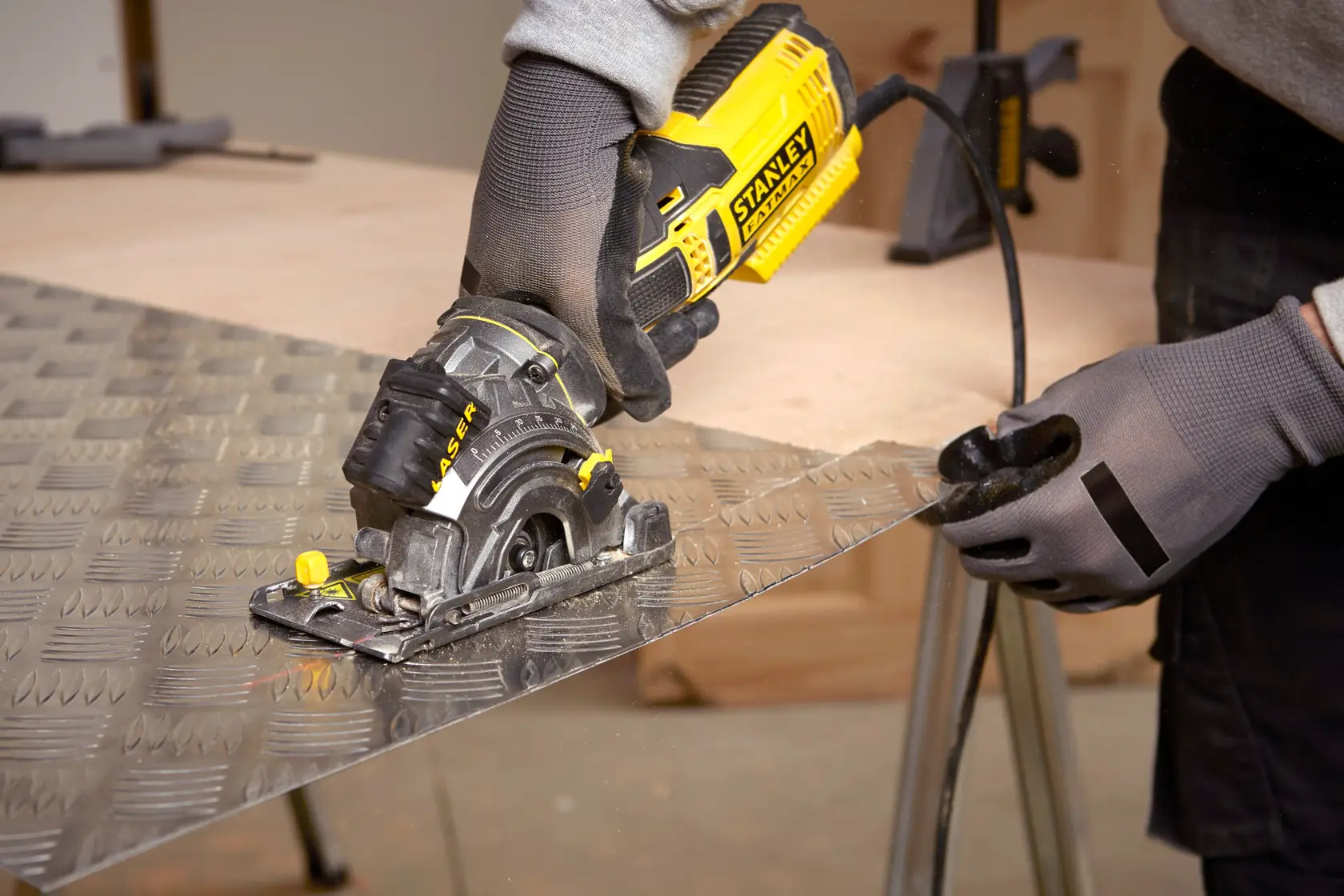 STANLEY FME380K kompakte Kreissäge schneidet Metallblech, Nahaufnahme mit behandschuhten Händen, Werkstattumgebung.