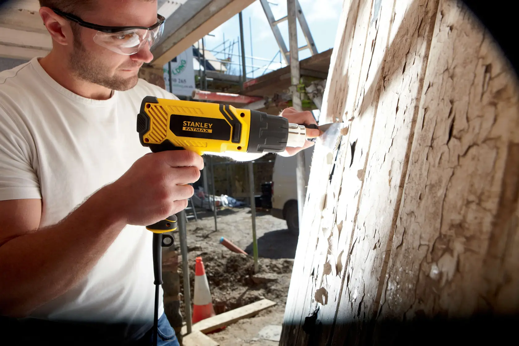 Foto der STANLEY FME670K Heißluftpistole beim Entfernen von Farbe auf Holz an einer Baustelle.