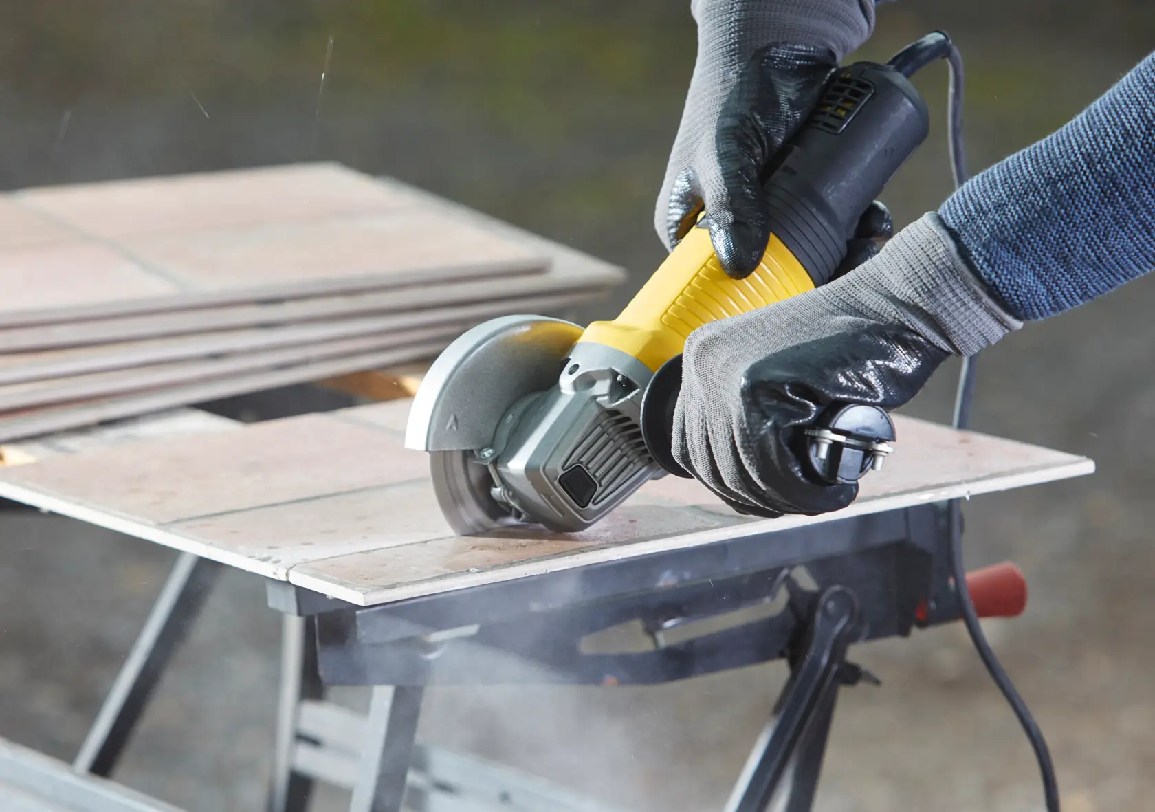 STANLEY FMEG220 Winkelschleifer schneidet Fliese, Nahaufnahme, schwarz-gelbes Werkzeug mit Handschuhen.