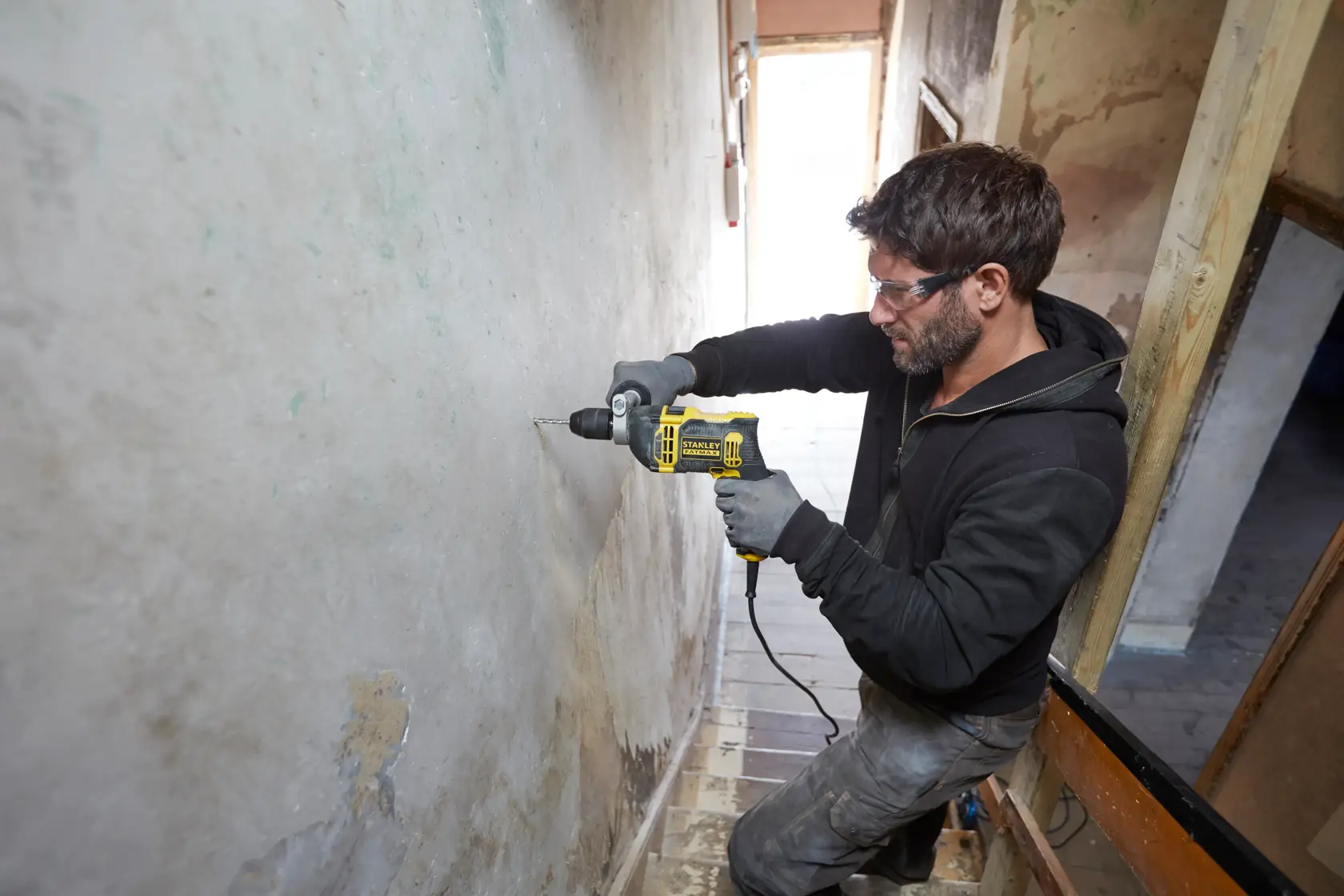 STANLEY FMEH750K kabelgebundene Schlagbohrmaschine im Einsatz beim Bohren in eine Wand, Produktfoto, Seitenansicht.