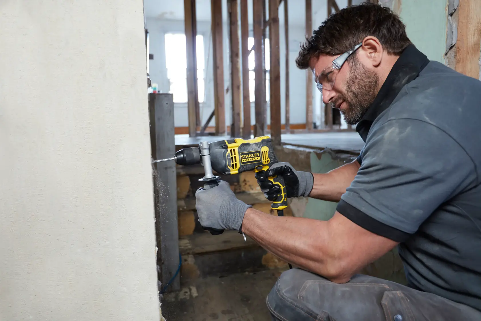 Foto eines Arbeiters mit STANLEY FMEH750K Schlagbohrmaschine, der eine Betonwand auf einer Baustelle bohrt.