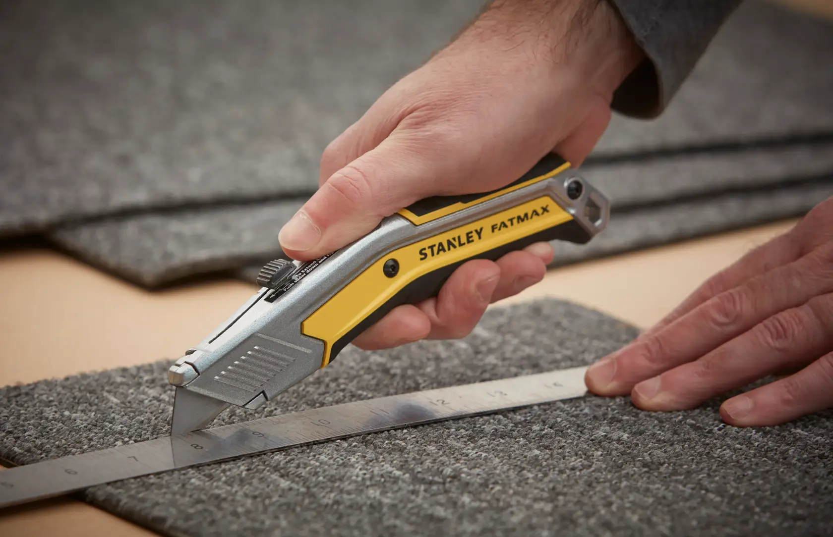 Foto des STANLEY FATMAX FMHT0-10288 Universalmessers, das Teppich entlang eines Metalllineals schneidet.