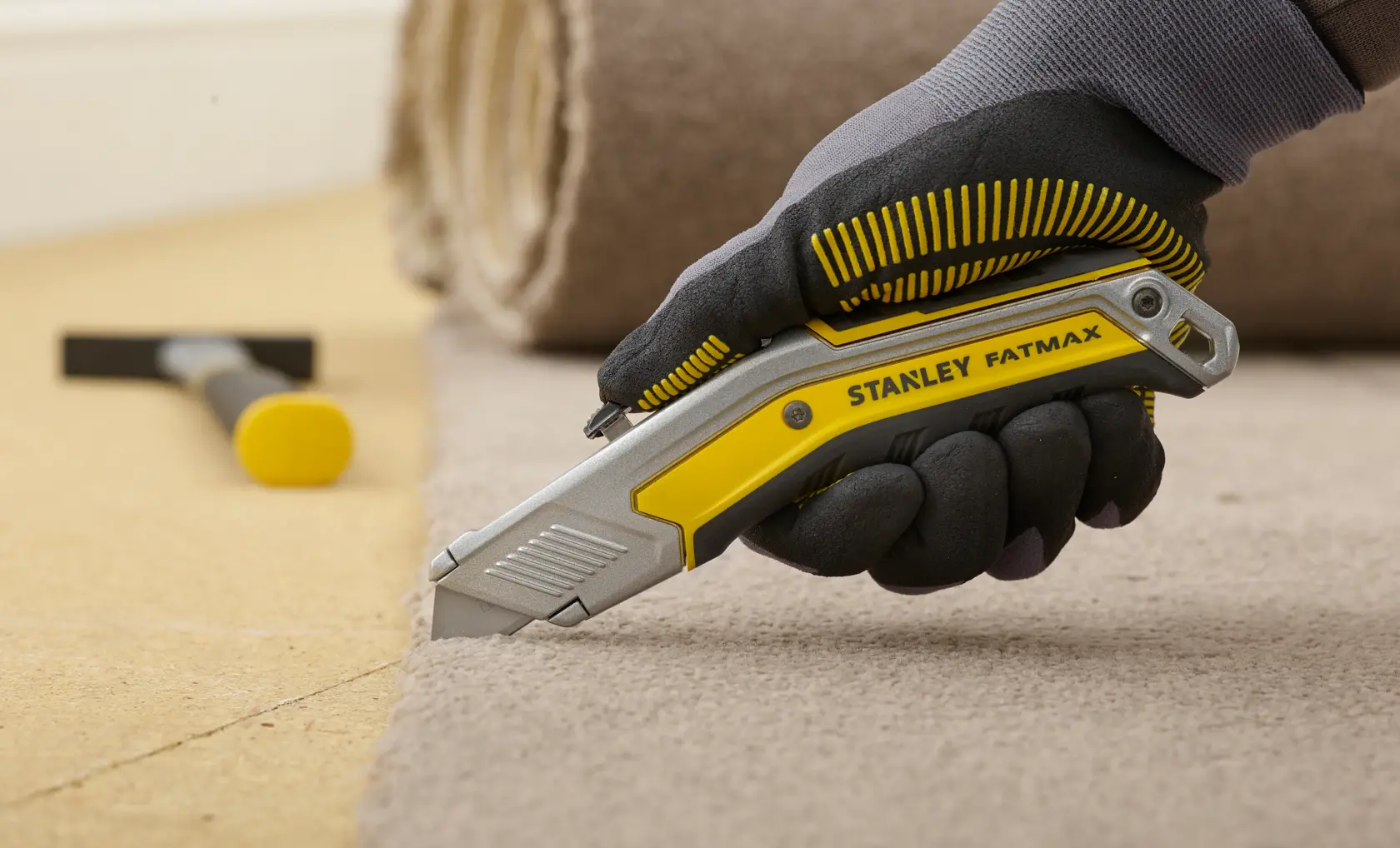 STANLEY FMHT0-10288 Universalmesser schneidet Teppich, ergonomischer gelb-silberner Griff, behandschuhte Hand.