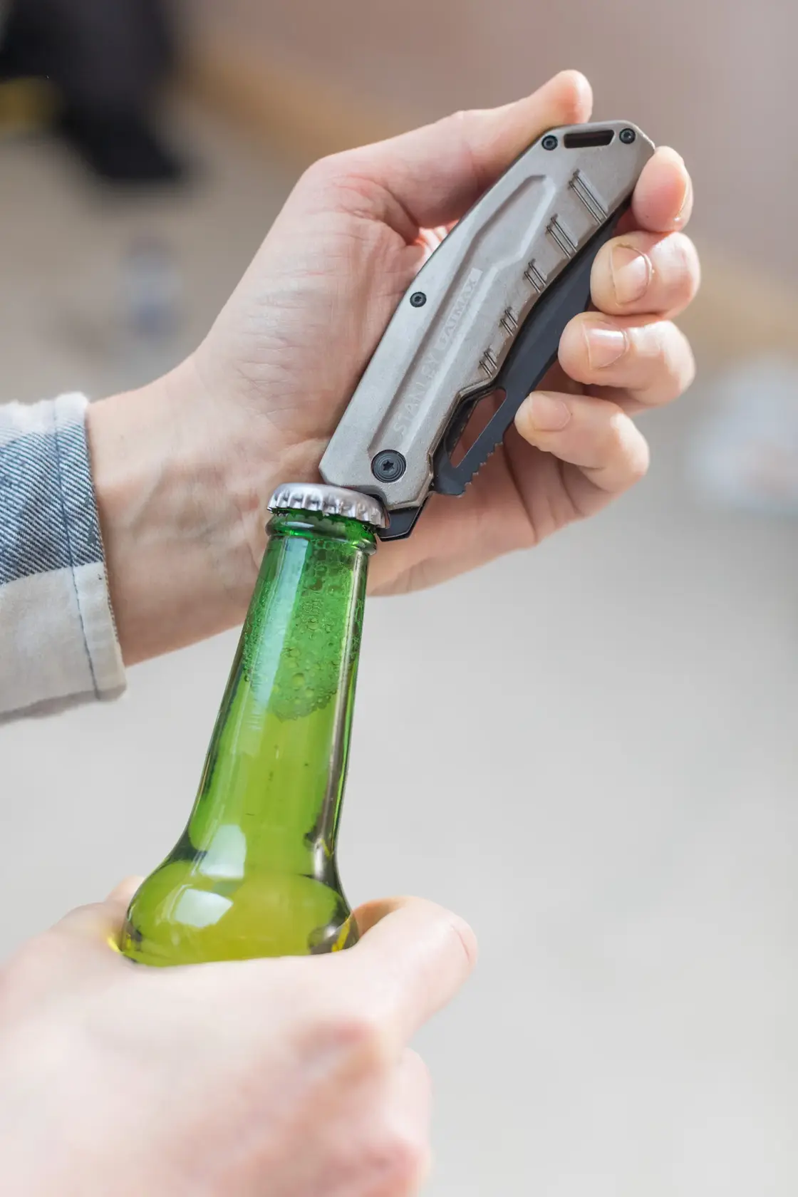 Foto des klappbaren STANLEY FMHT0-10312 Universalmessers beim Öffnen einer grünen Glasflasche.