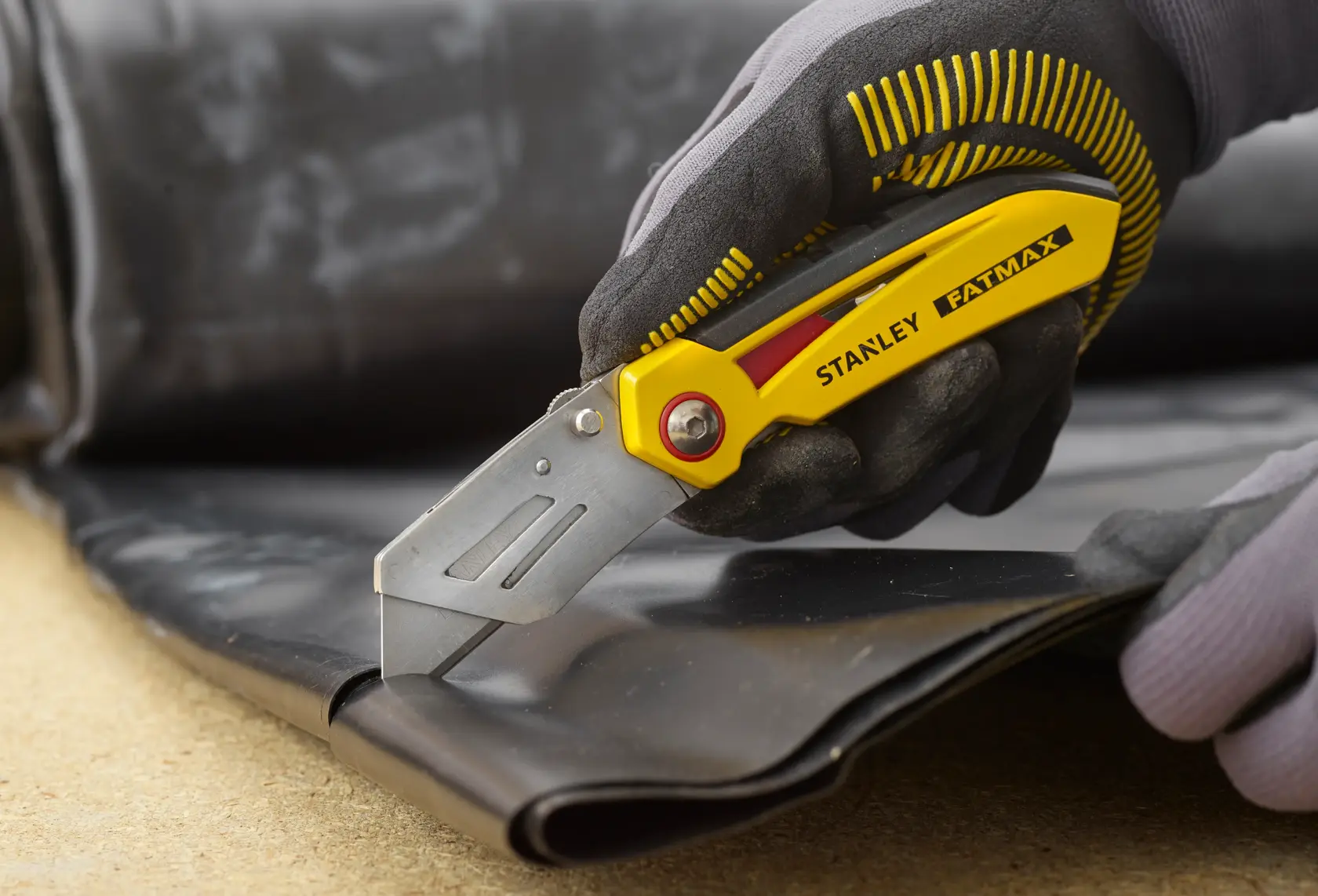 Stanley FMHT0-10827 Cuttermesser schneidet schwarzes Material, Nahaufnahme, gelbes und silbernes Design.