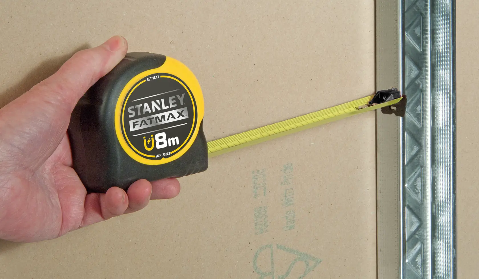 Foto vom STANLEY FMHT0-33868 FATMAX 8m Maßband im Einsatz an einer Wand neben einem Metallprofil.